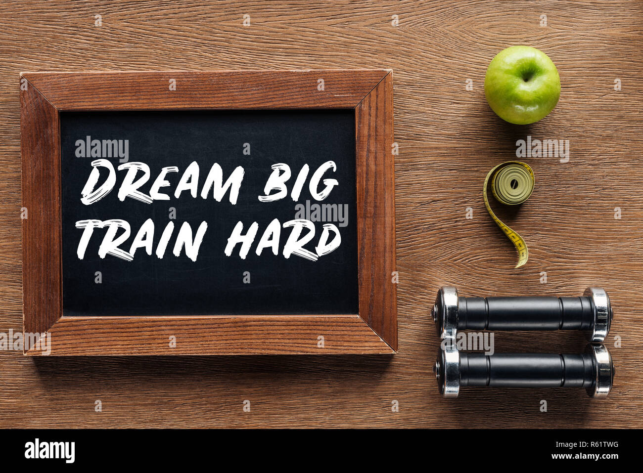 apple, dumbbells, measuring tape and wooden chalk board with 'dream big train hard' quote, dieting and healthy lifesyle concept Stock Photo