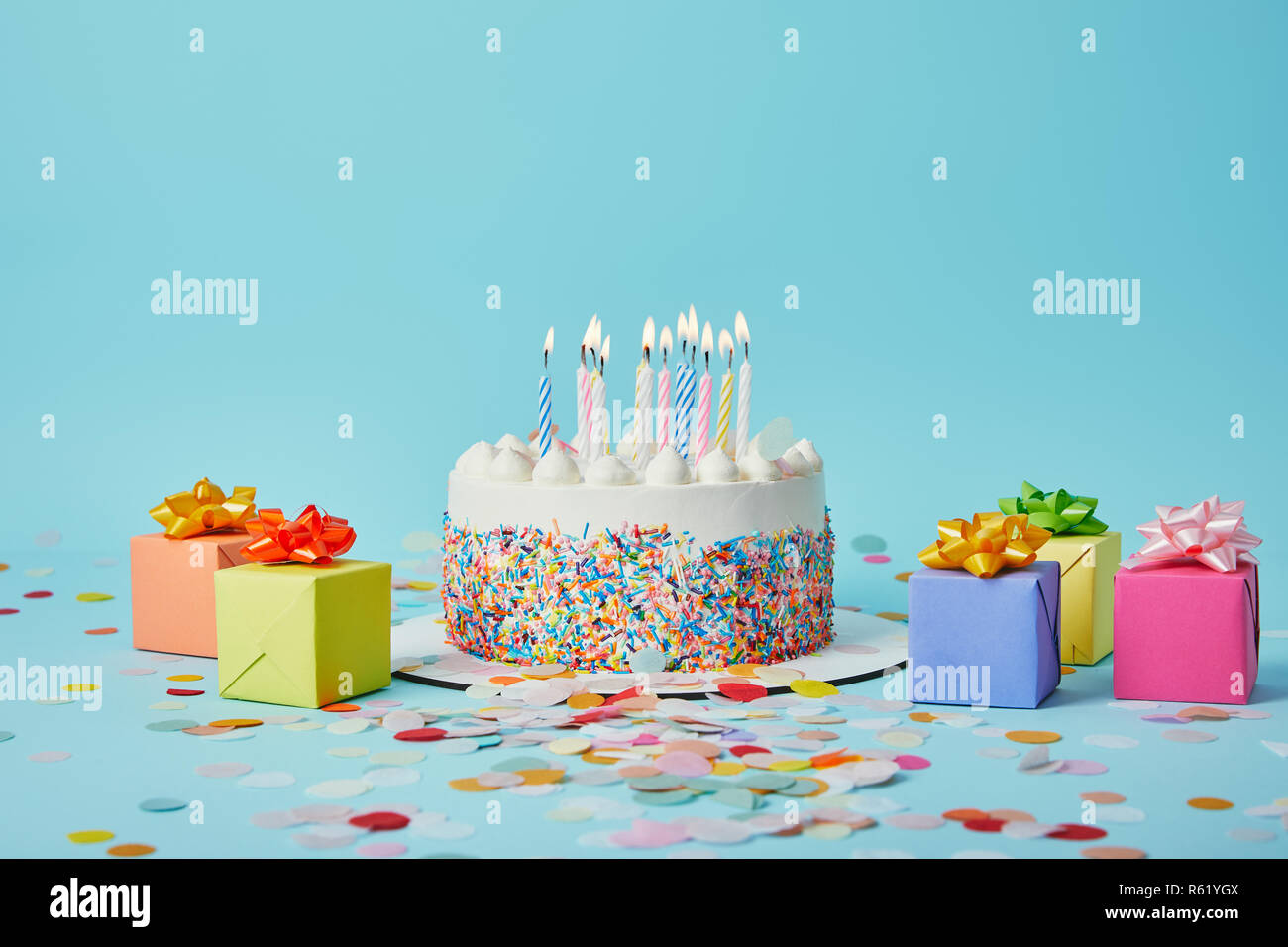 Delicious cake with candles, colorful gifts and confetti on blue ...