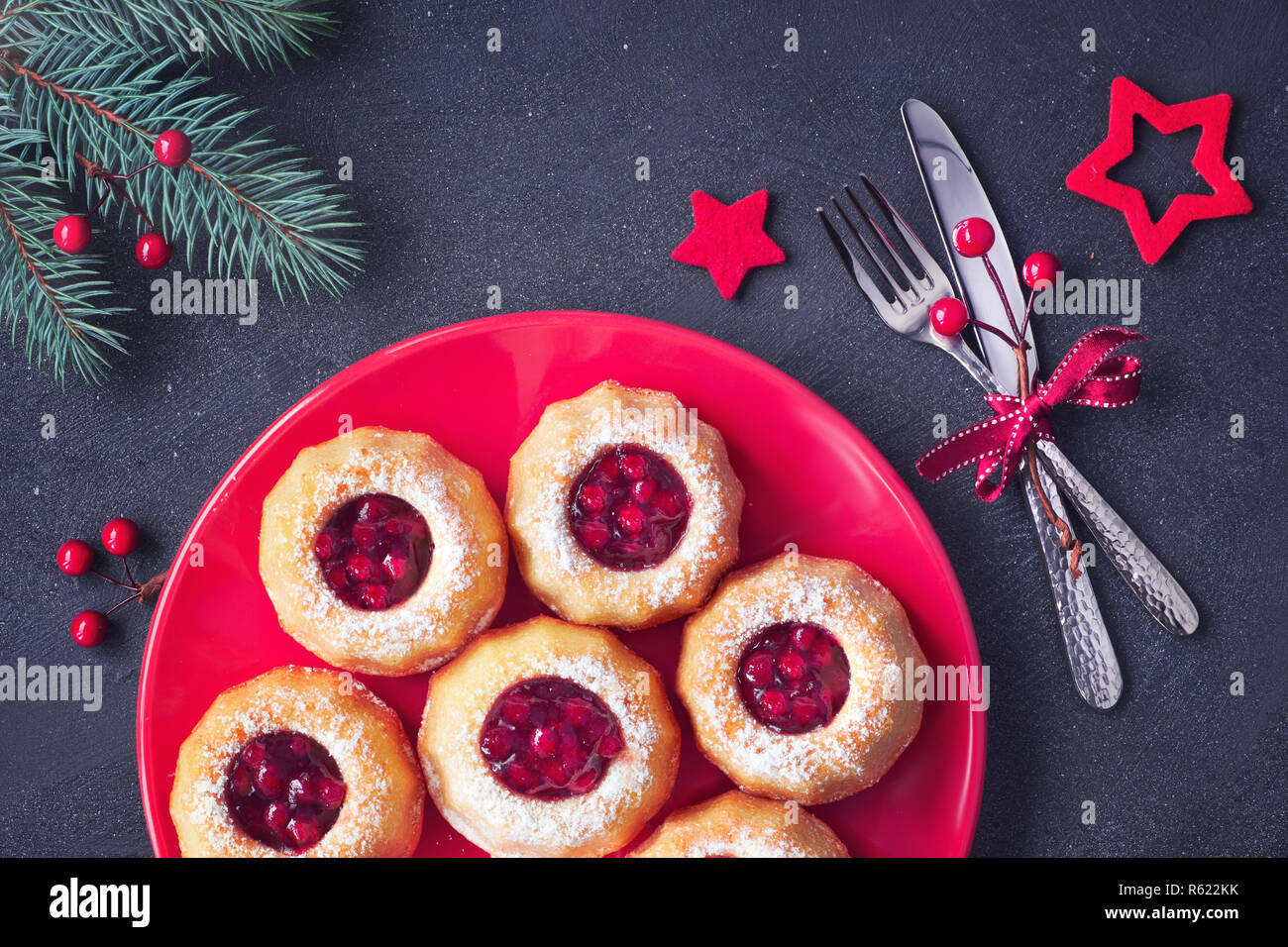 Mini bundt ring cakes with red whortleberry jam on dark background with fir twigs and berries. Christmas holiday sweet food. Stock Photo