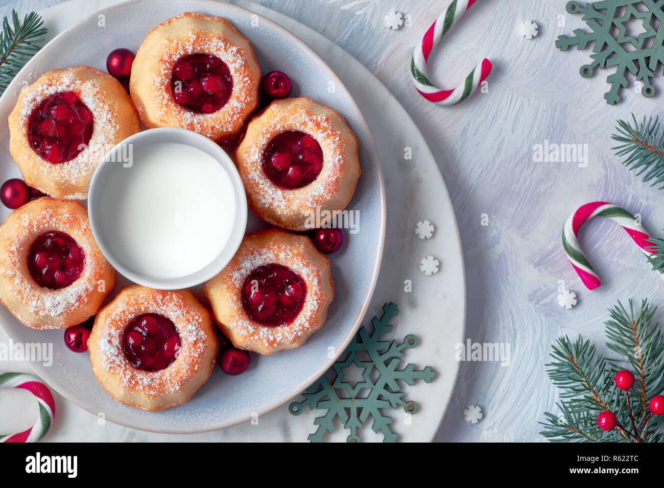 Mini bundt ring cakes with red whortleberry jam on light background with fir twigs, berries and candy canes. Christmas holiday sweet food. Stock Photo