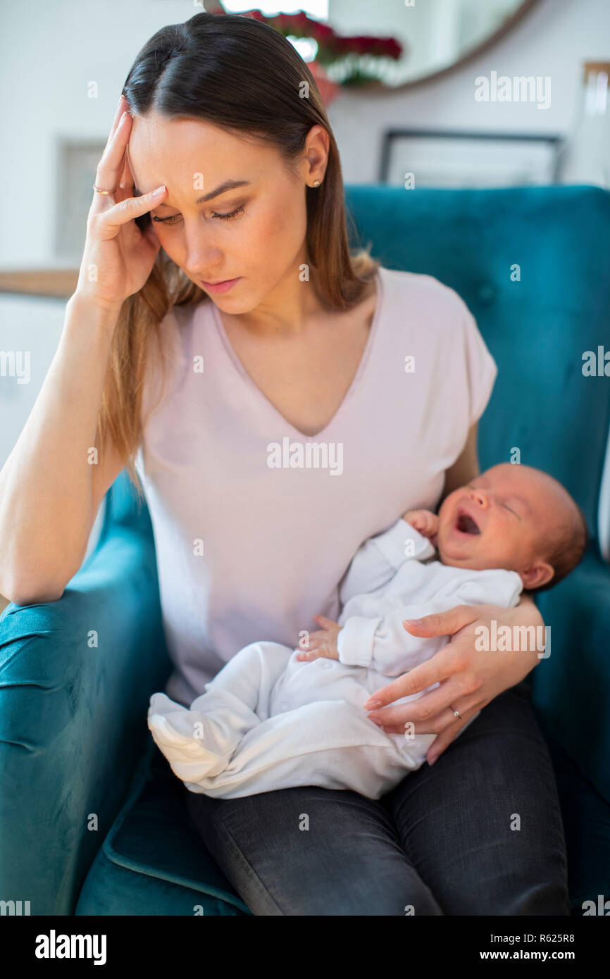 Stressed Mother Holding Crying Baby Suffering From Post Natal Depression At Home Stock Photo