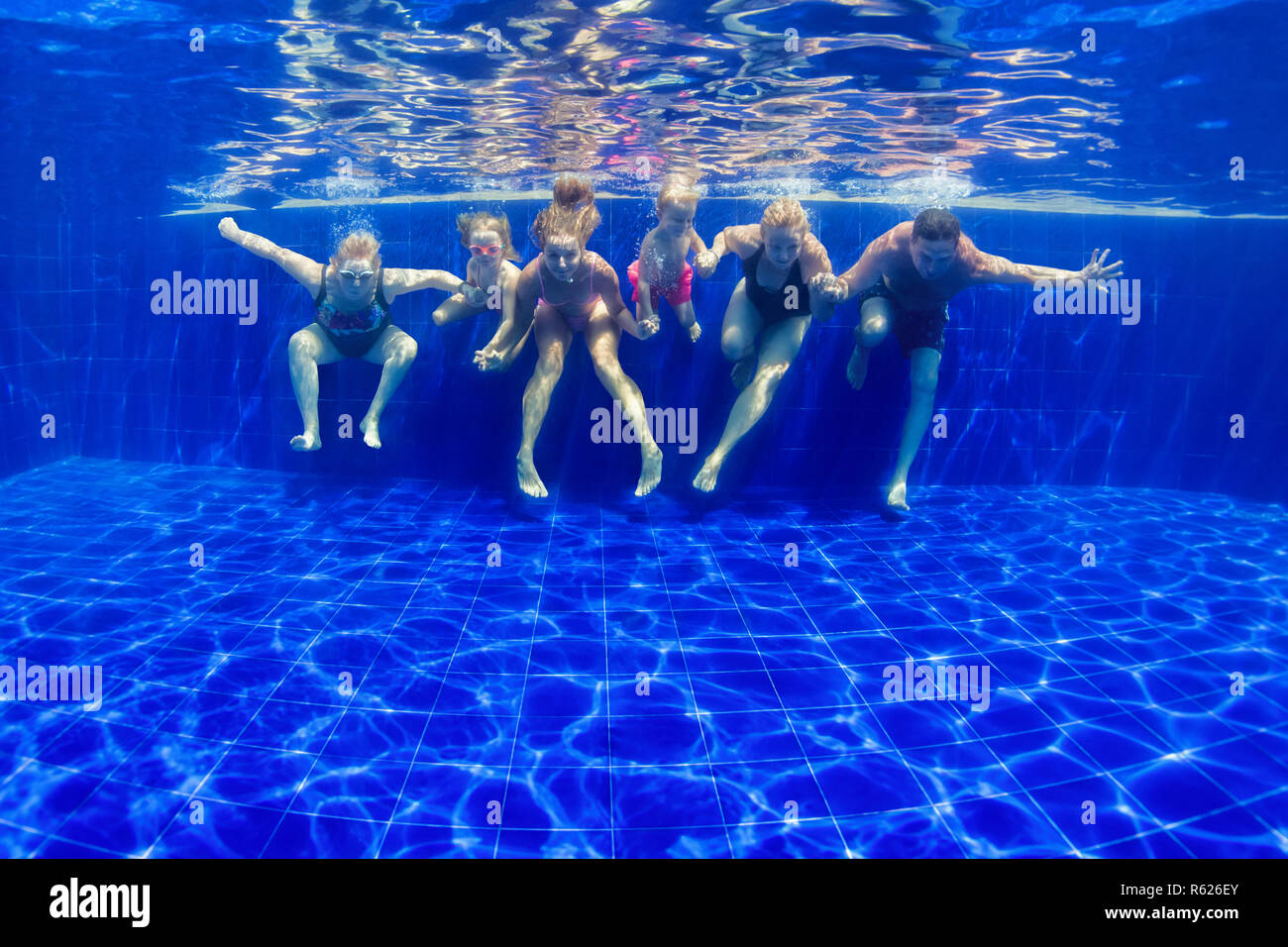 Happy family in swimming pool. Smiling mother, children and grandparents swim, dive in pool with fun - jump deep down underwater. Stock Photo