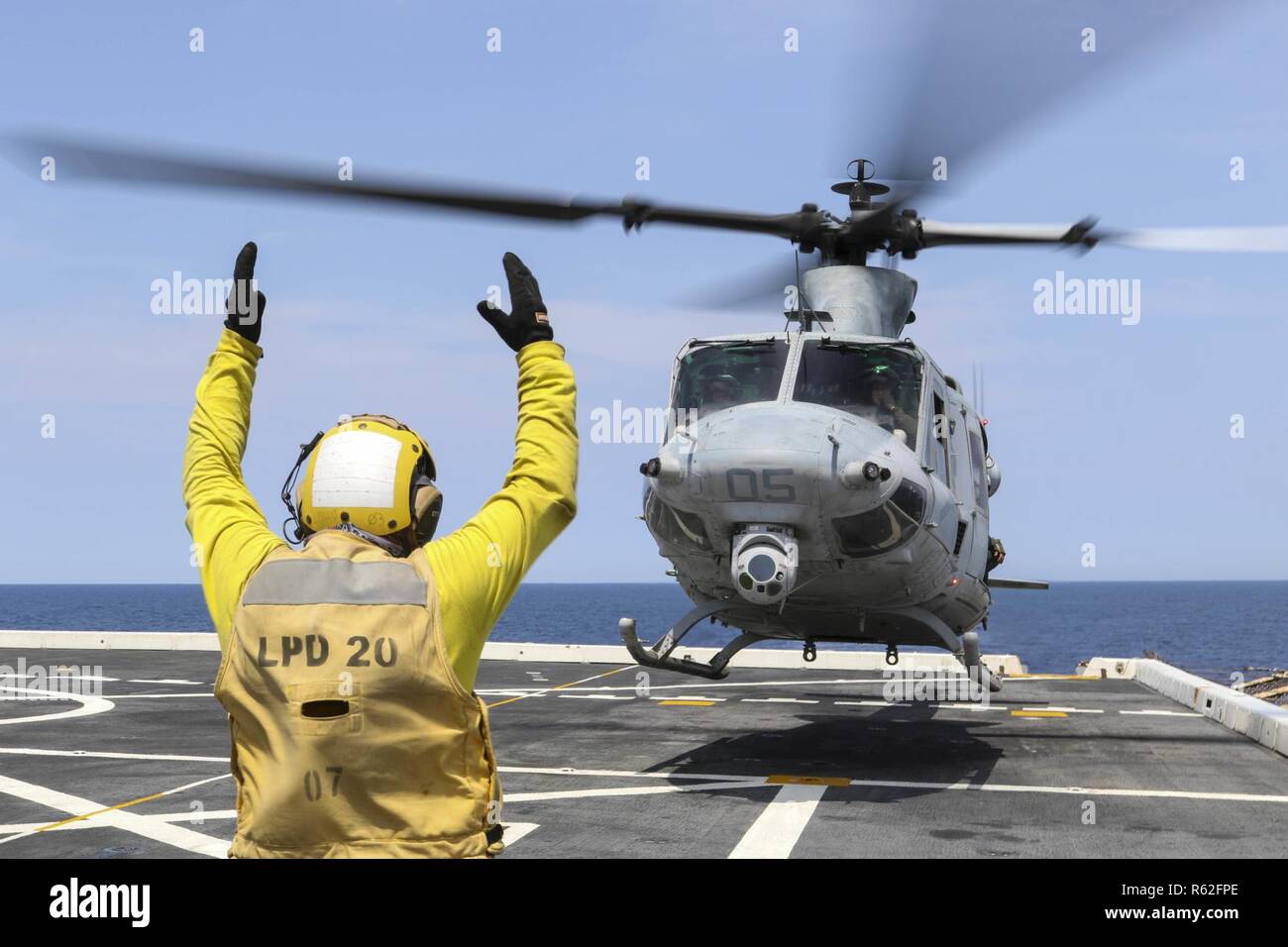 CORAL SEA (Nov. 19, 2018) Aviation Boatswain’s Mate (Handling) 3rd Class Walter Rutherford, from Cheyenne, Wyo., signals a UH-1Y Huey helicopter, assigned to Marine Light Attack Helicopter Squadron (HMLA) 469, as it takes off from the flight deck of the amphibious transport dock ship USS Green Bay (LPD 20) prior to cross deck flight operations with the Royal Australian Navy helicopter landing dock ship HMAS Adelaide (L01). Green Bay, part of Commander Amphibious Squadron 11, is operating in the region to enhance interoperability with partners and serve as a ready-response force for any type of Stock Photo