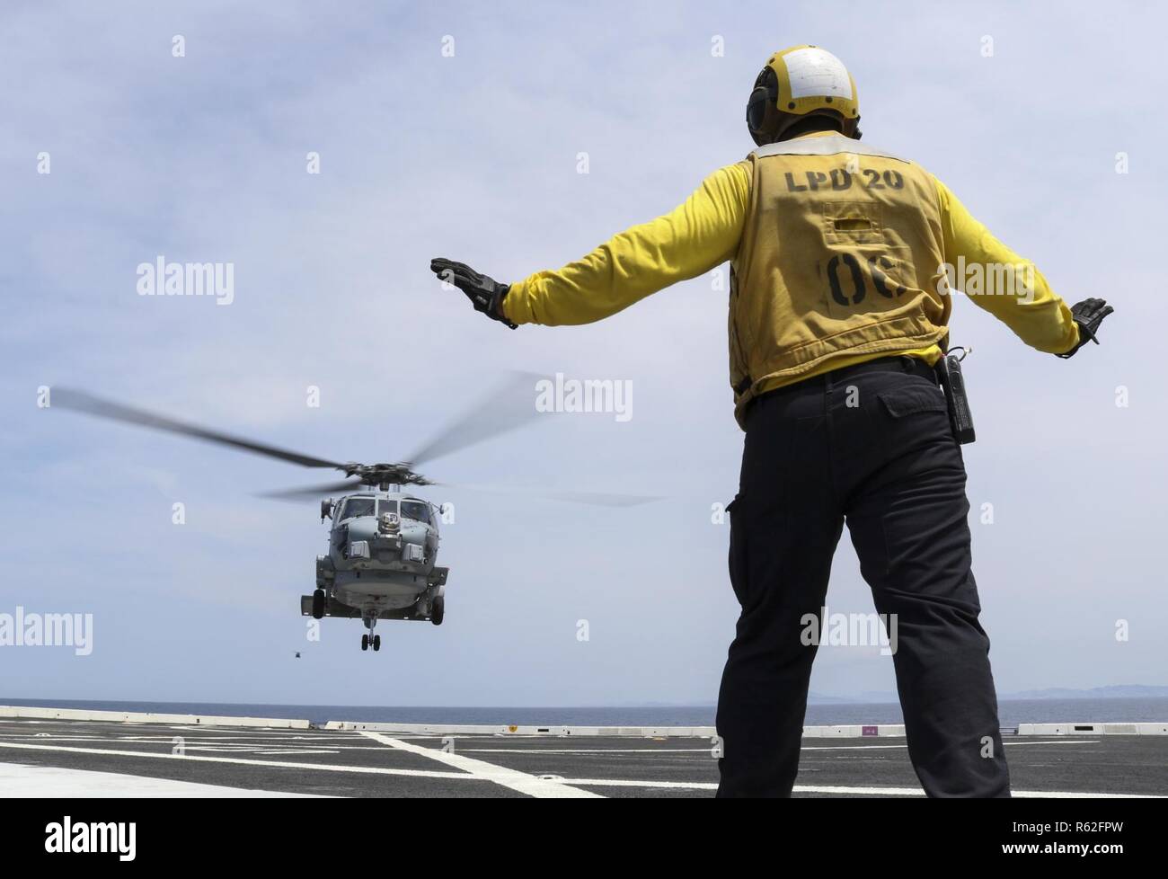 CORAL SEA (Nov. 19, 2018) Aviation Boatswain’s Mate (Handling) 3rd Class Dion Sanders, from New York, signals a MH-60R Seahawk helicopter, assigned to the Royal Australian Navy helicopter landing dock ship HMAS Adelaide (L01), as it lands on the flight deck of the amphibious transport dock ship USS Green Bay (LPD 20) during cross deck flight operations. Green Bay, part of Commander Amphibious Squadron 11, is operating in the region to enhance interoperability with partners and serve as a ready-response force for any type of contingency. Stock Photo