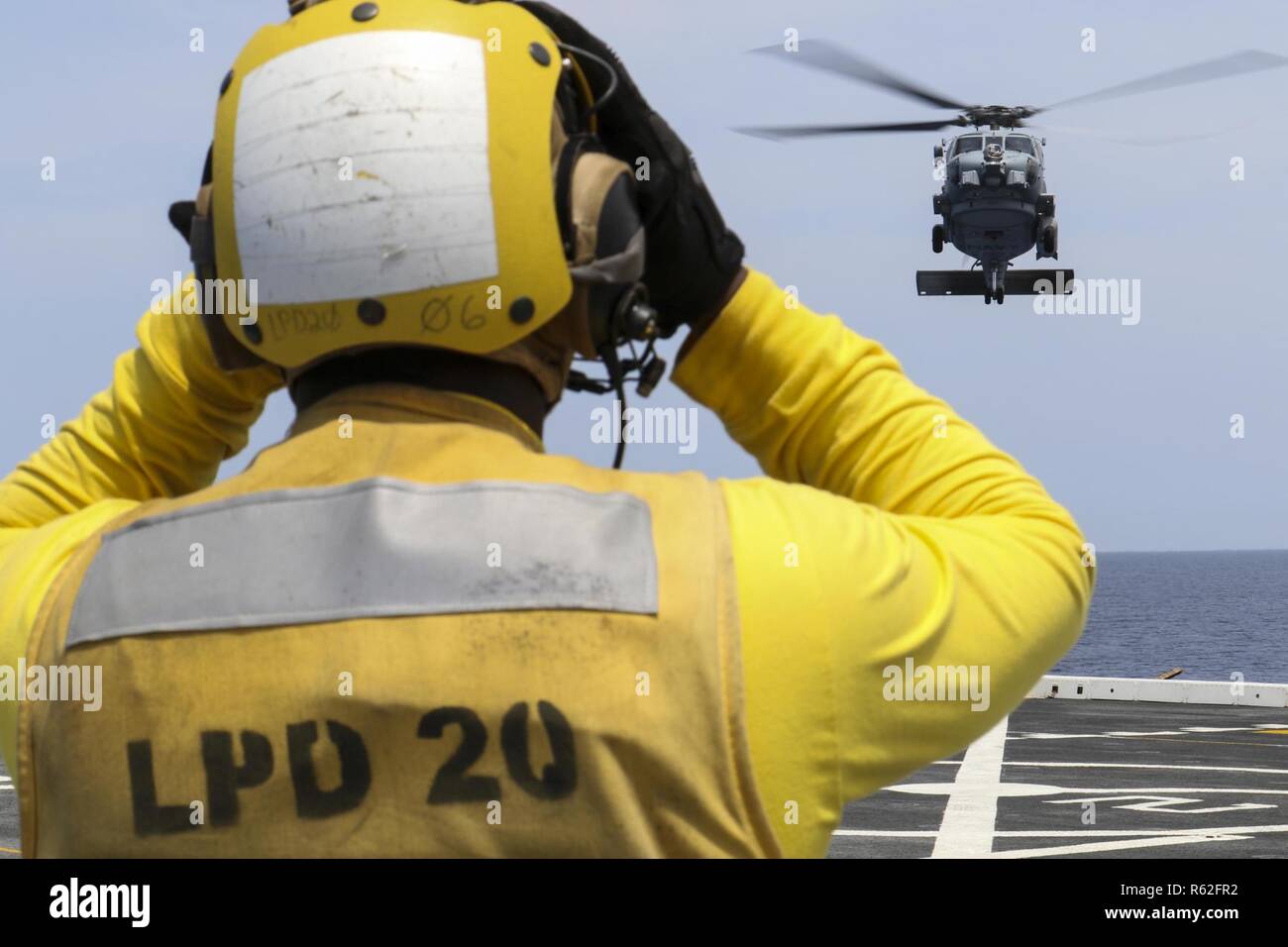 CORAL SEA (Nov. 19, 2018) Aviation Boatswain’s Mate (Handling) 3rd Class Dion Sanders, from New York, signals a MH-60R Seahawk helicopter, assigned to the Royal Australian Navy helicopter landing dock ship HMAS Adelaide (L01), as it lands on the flight deck of the amphibious transport dock ship USS Green Bay (LPD 20) during cross deck flight operations. Green Bay, part of Commander Amphibious Squadron 11, is operating in the region to enhance interoperability with partners and serve as a ready-response force for any type of contingency. Stock Photo