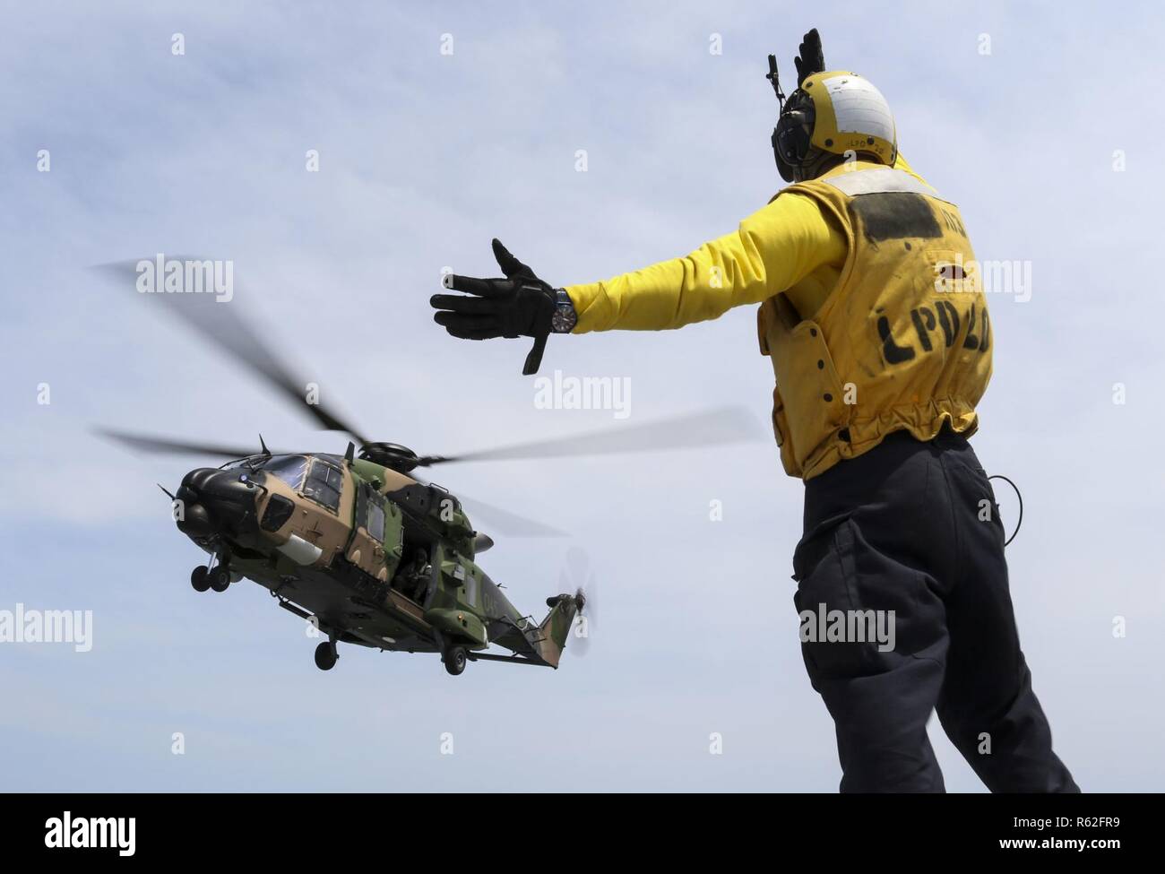 CORAL SEA (Nov. 19, 2018) Aviation Boatswain’s Mate (Handling) Airman Caleb Brawner, from Wichita, Kan., signals a MRH-90 Taipan helicopter, assigned to the Royal Australian Navy helicopter landing dock ship HMAS Adelaide (L01), as it takes off from the flight deck of the amphibious transport dock ship USS Green Bay (LPD 20) during cross deck flight operations. Green Bay, part of Commander Amphibious Squadron 11, is operating in the region to enhance interoperability with partners and serve as a ready-response force for any type of contingency. Stock Photo