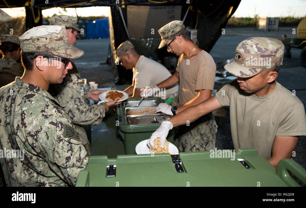 TINIAN, Commonwealth of the Northern Mariana Islands (Nov. 18, 2018) Army Spc. Angelito Angala, assigned to the 303rd Maneuver Enhancement Brigade, from Honolulu, and Construction Mechanic Construction Apprentice James Joyce, assigned to Naval Mobile Construction Battalion (NMCB) 1, Detachment Guam, from Pittsburgh, serve dinner to Sailors assigned to NMCB 1 during recovery efforts. Service members from Joint Region Marianas and U.S. Indo-Pacific Command are providing Department of Defense support to the Commonwealth of the Northern Mariana Islands' civil and local officials as part of the Fed Stock Photo