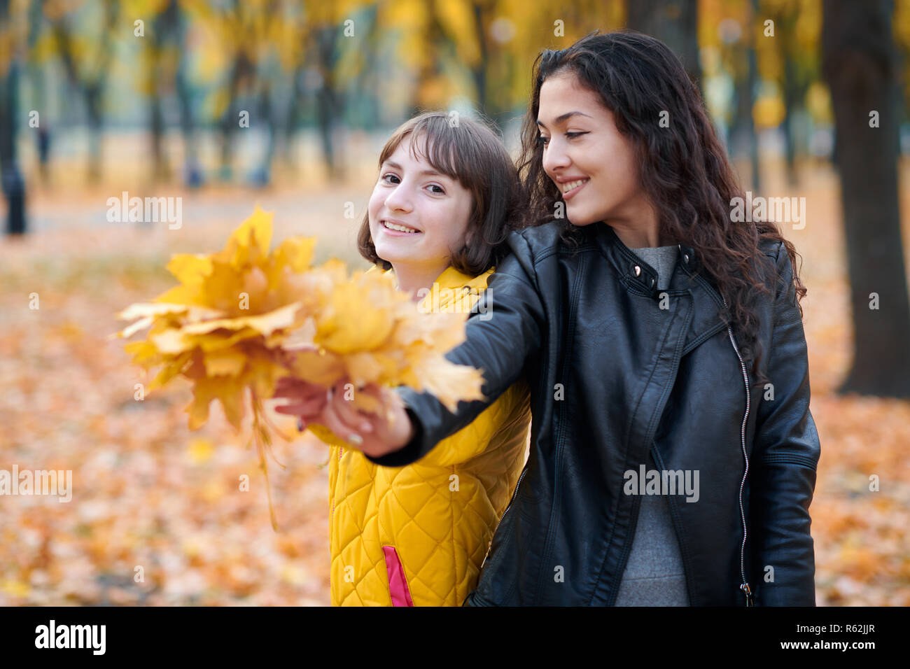 Pretty woman and teen girl are posing with bunch of maple's leaves in ...