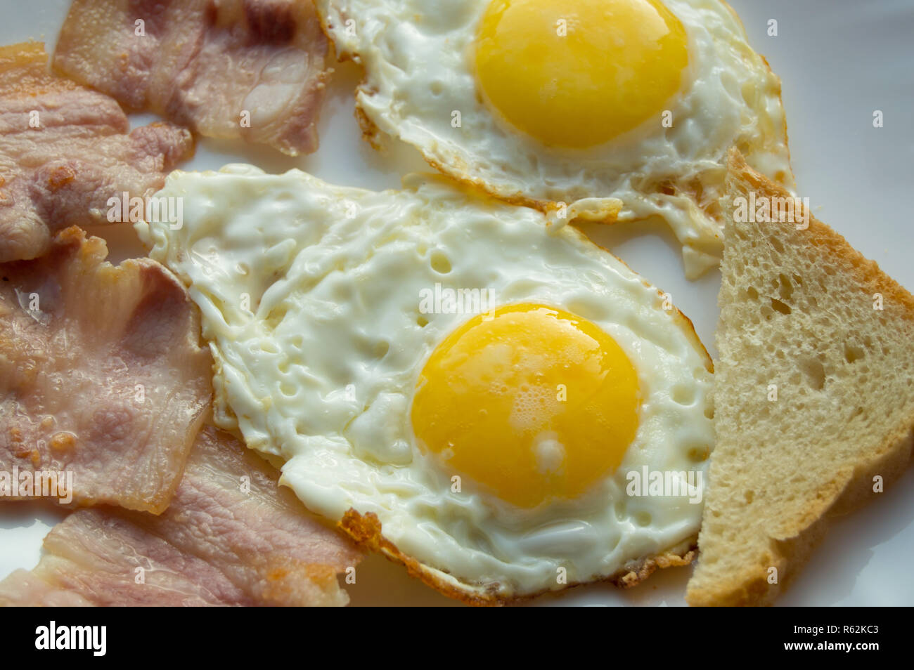Delicious Breakfast - white plate of fried eggs, bacon and toast Stock Photo