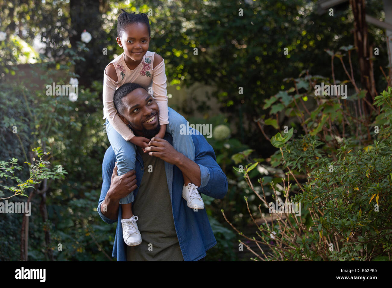 A girl sitting on her fathers shoulders in a garden Stock Photo