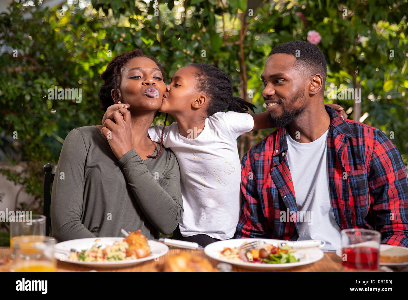 A family eating together, daughter kissing mother on the cheek Stock Photo