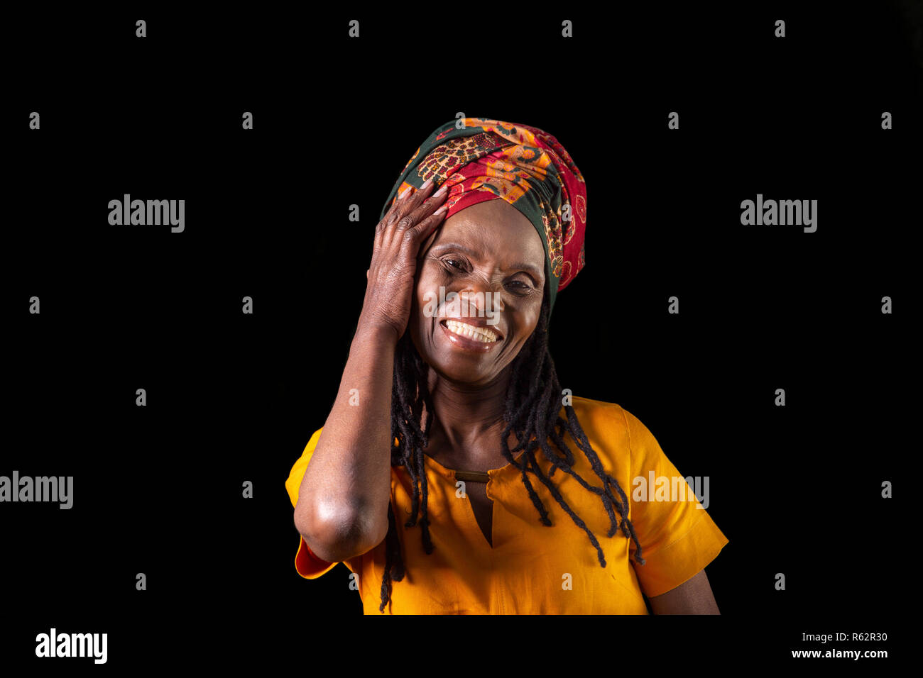 Closeup of an elderly African woman smiling and wearing a headscarf against a black background Stock Photo