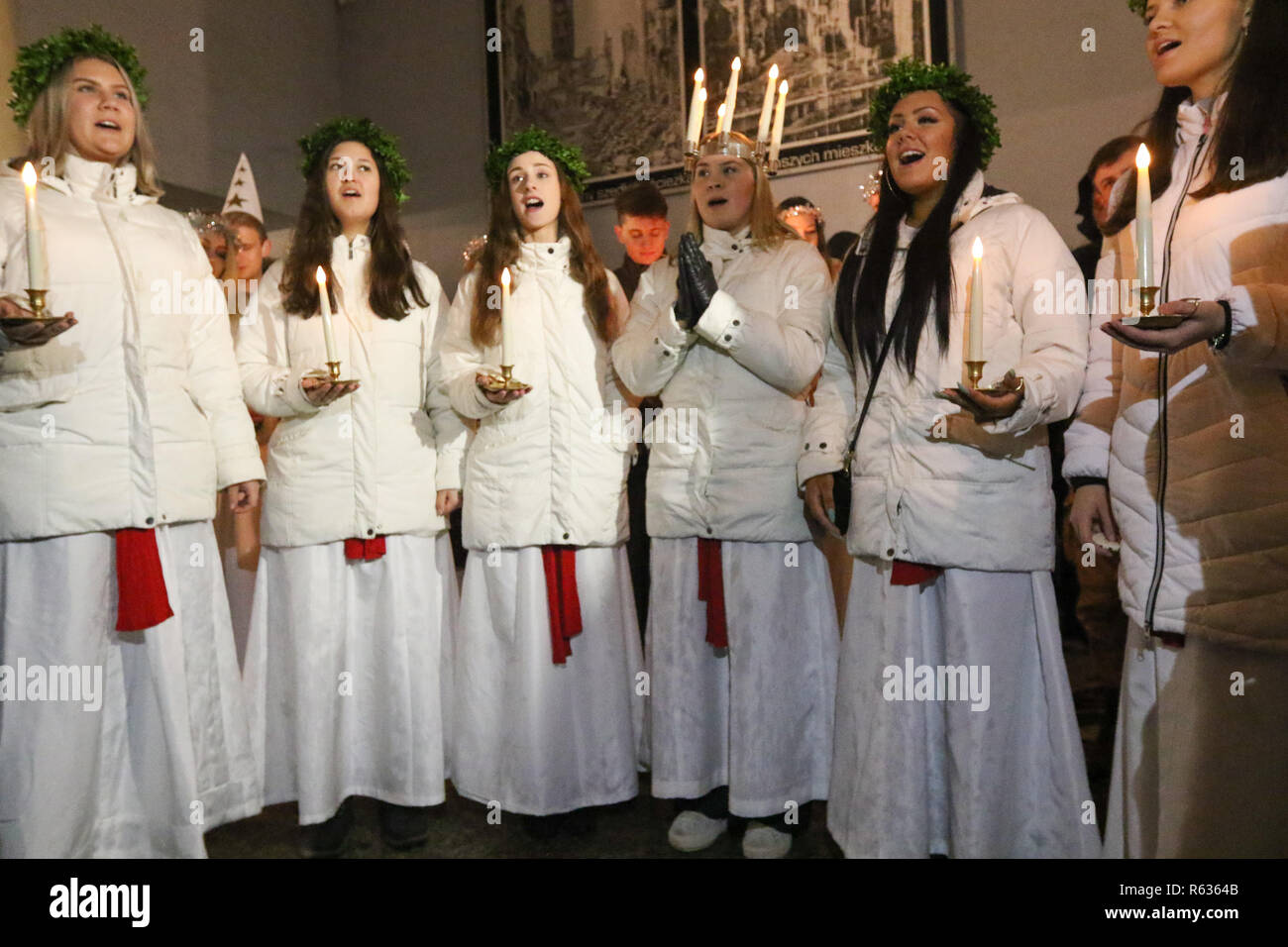 Gdansk, Poland 3rd. December 2018 Young girls from Kalmar, Sweden dressed in a white dress and a red sash (as the symbol of martyrdom) carrying candles singing in the Gdansk Old City centre. Swedish girls dressed as Saint Lucy (Sankta Lucia)  carry cookies in procession and sing a songs. It is said that to vividly celebrate St. Lucy's Day will help one live the long winter days with enough light  Credit: Max Ardulf/Alamy Live News Stock Photo