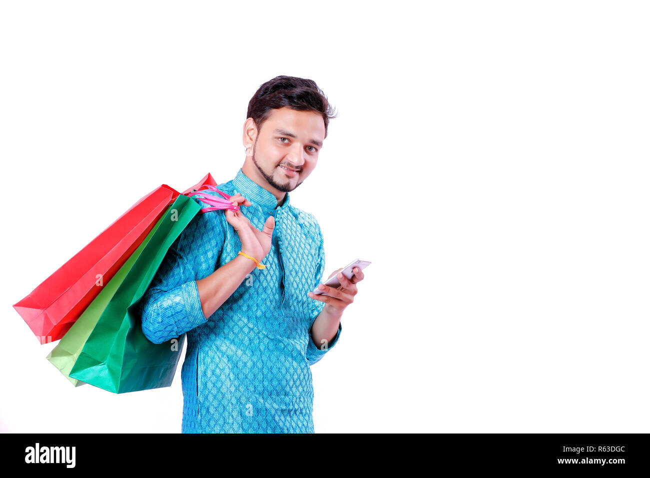 Indian man in ethnic wear with shopping bags and showing mobile screen , isolated over white background Stock Photo