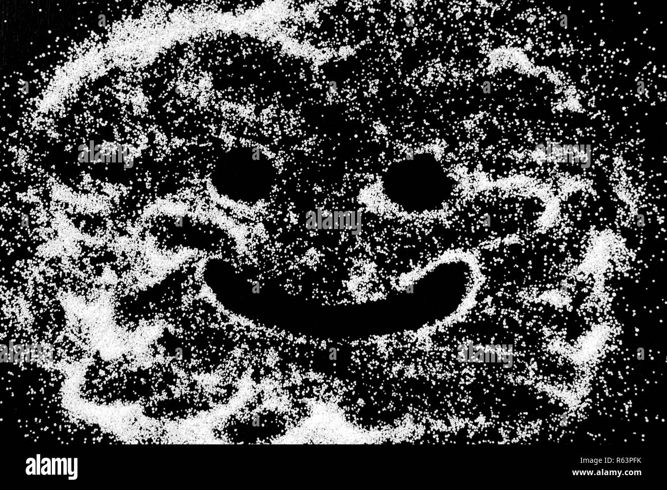 Symbol happy smile emoticon drawing by finger on white snow salt powder on black background. Concept with place for text. Copy space. Stock Photo