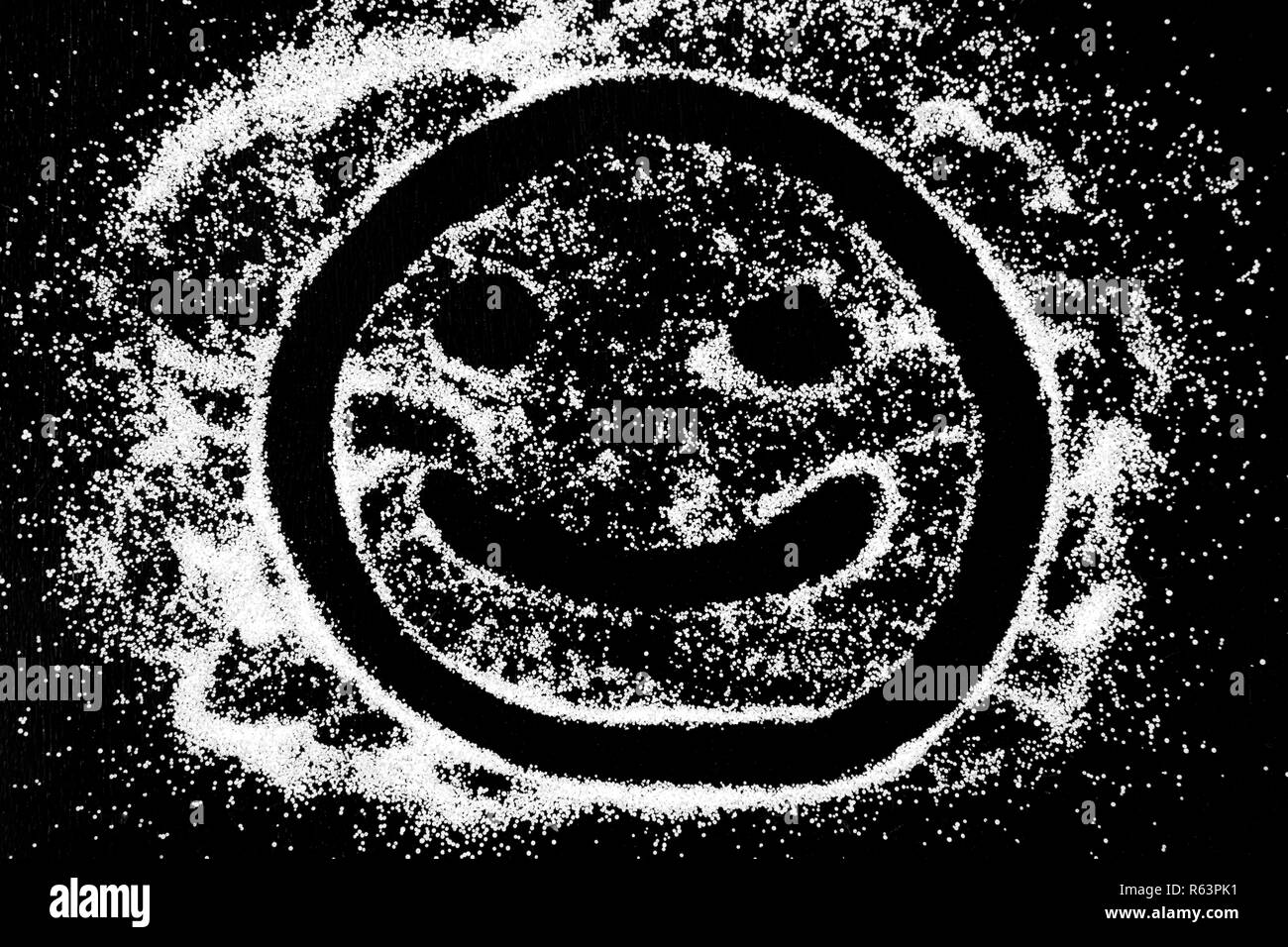 Symbol happy smile emoticon drawing by finger on white snow salt powder on black background. Concept with place for text. Copy space. Stock Photo