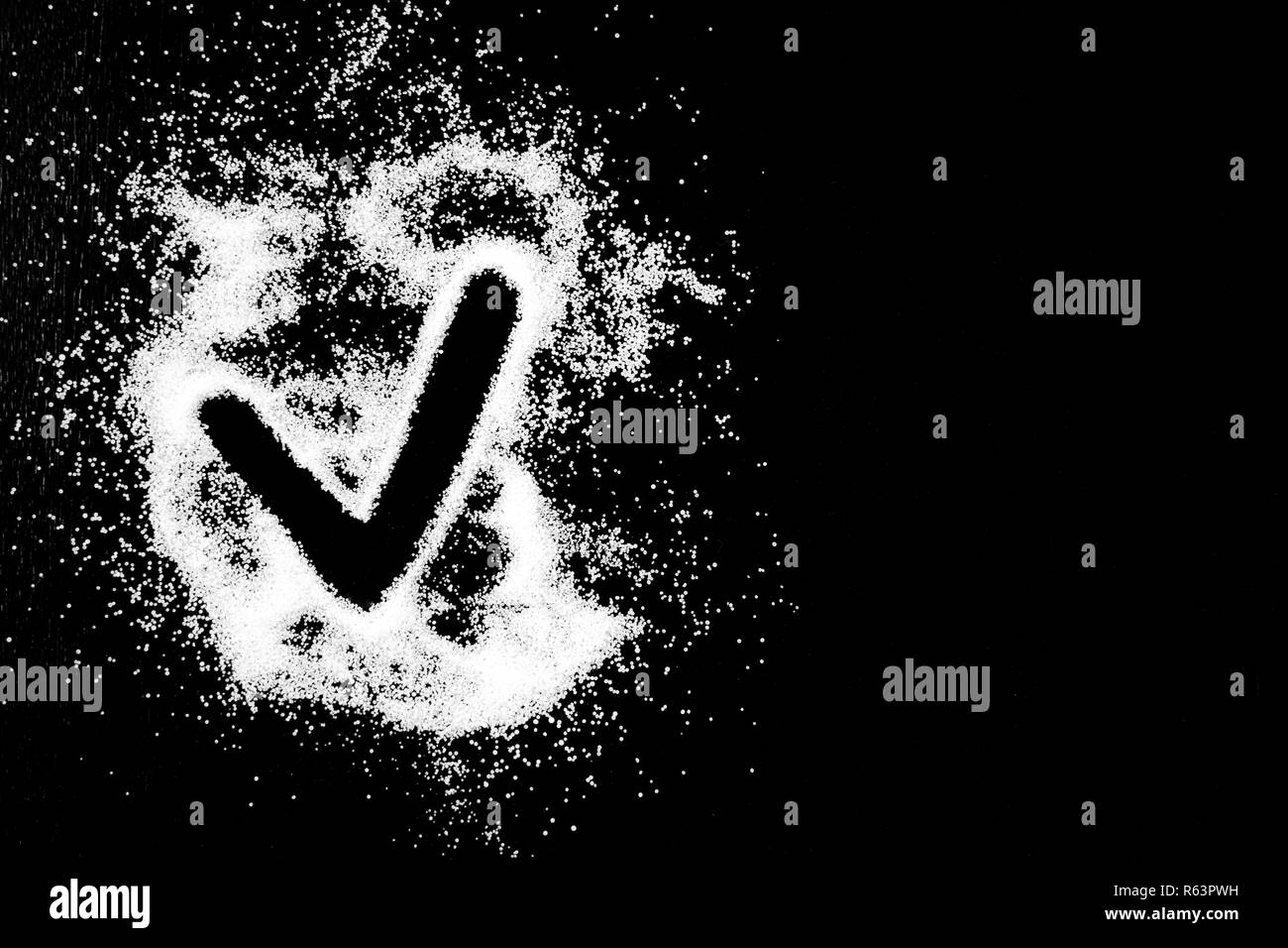 Checking mark symbol drawing by finger on white snow salt powder spot cloud on the left side on black background. Tick concept with place for text. Copy space. Stock Photo