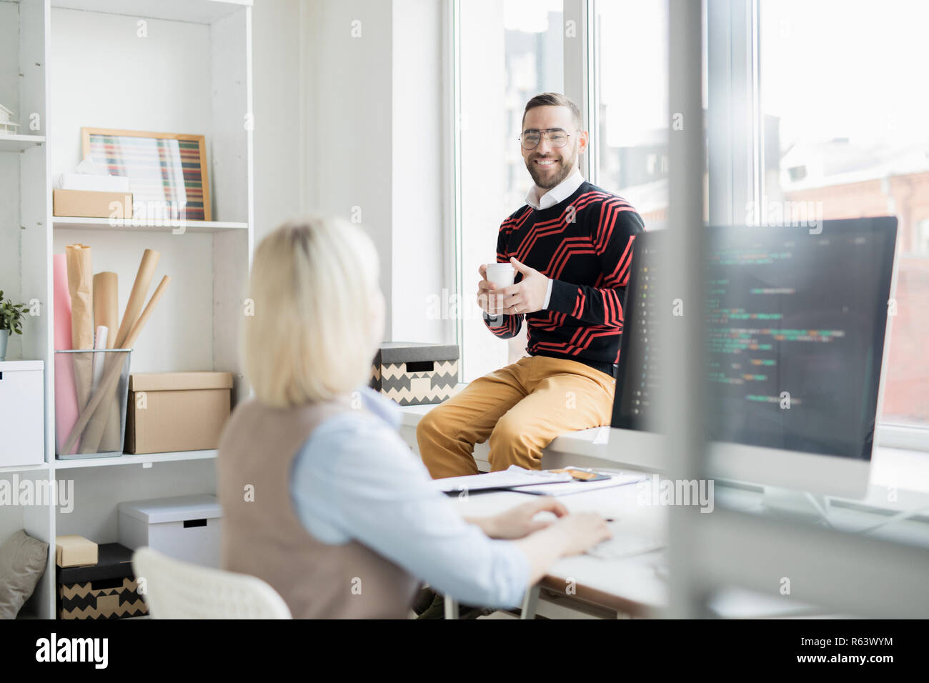 Cheerful office man drinking coffee while talking to coder Stock Photo