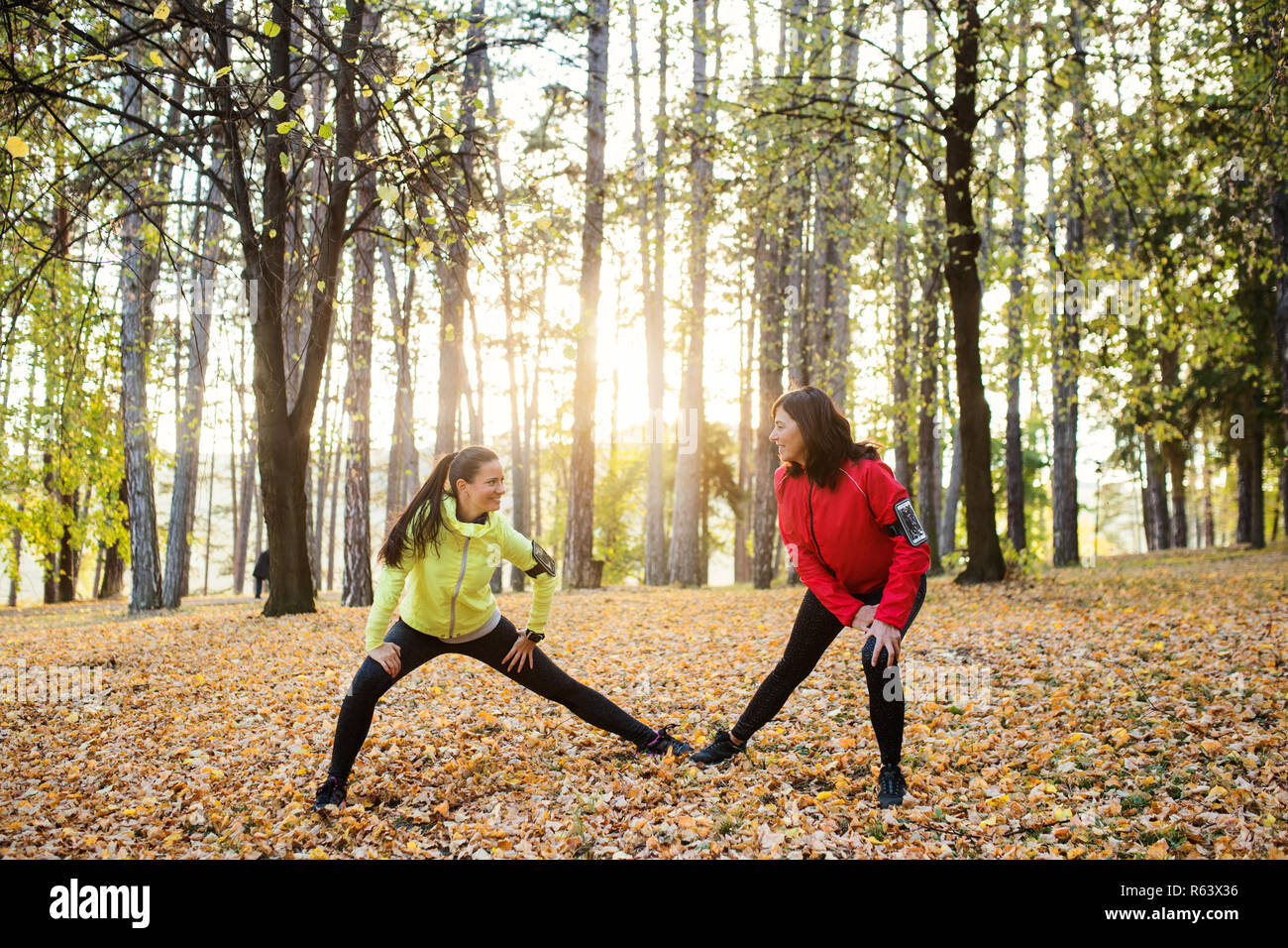 Two female runners stretching outdoors in forest in autumn nature. Stock Photo