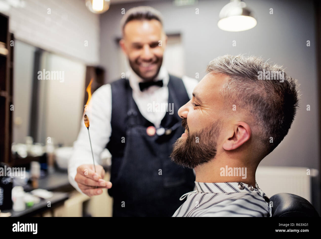 Hipster man client visiting haidresser and hairstylist in barber shop, ear hair removal. Stock Photo
