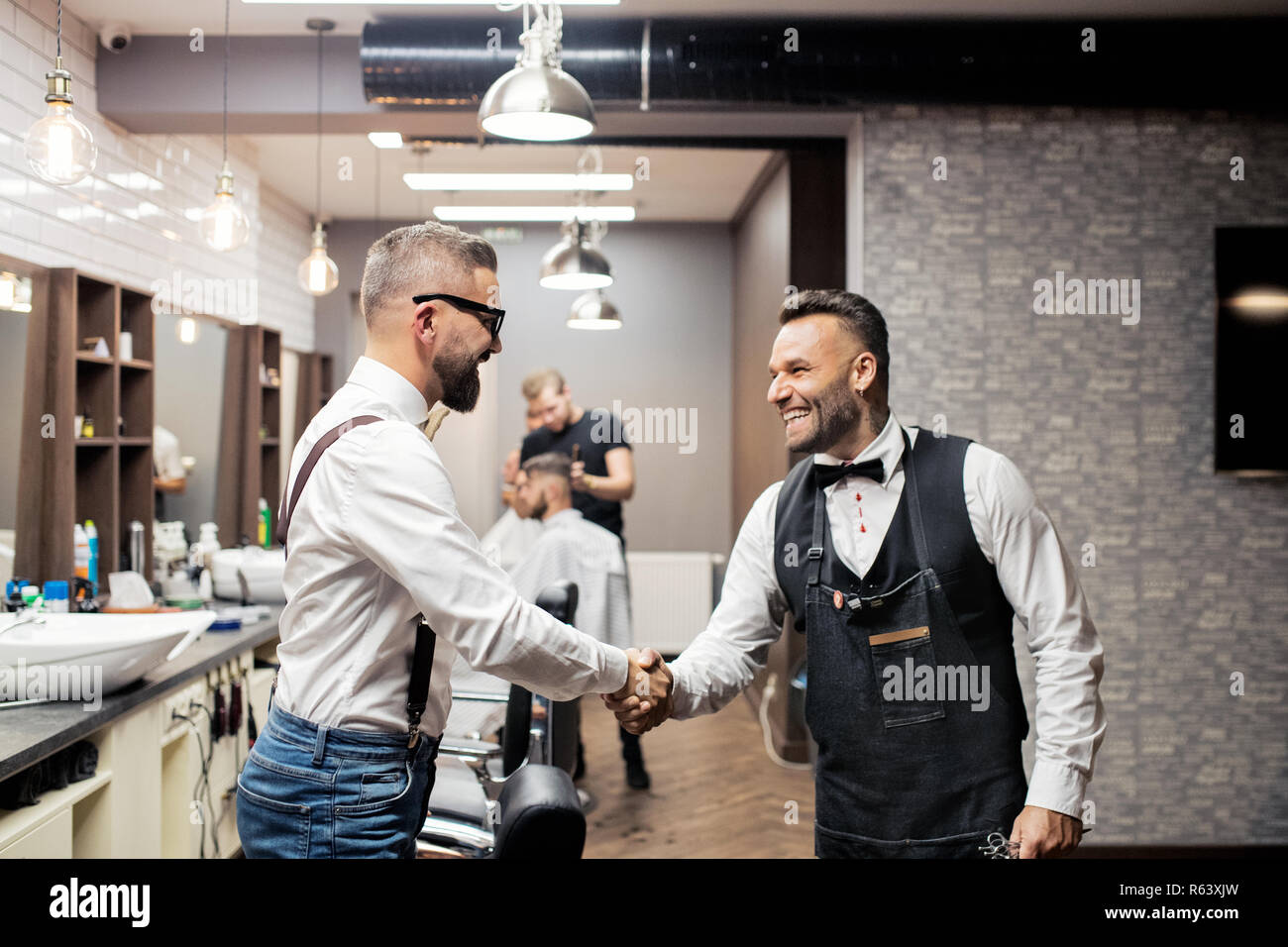 Hipster man client shaking hands with haidresser and hairstylist in barber shop. Stock Photo