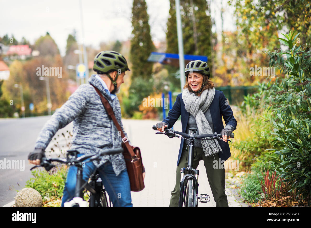 Active senior couple with electrobikes standing outdoors on pathway in town. Stock Photo