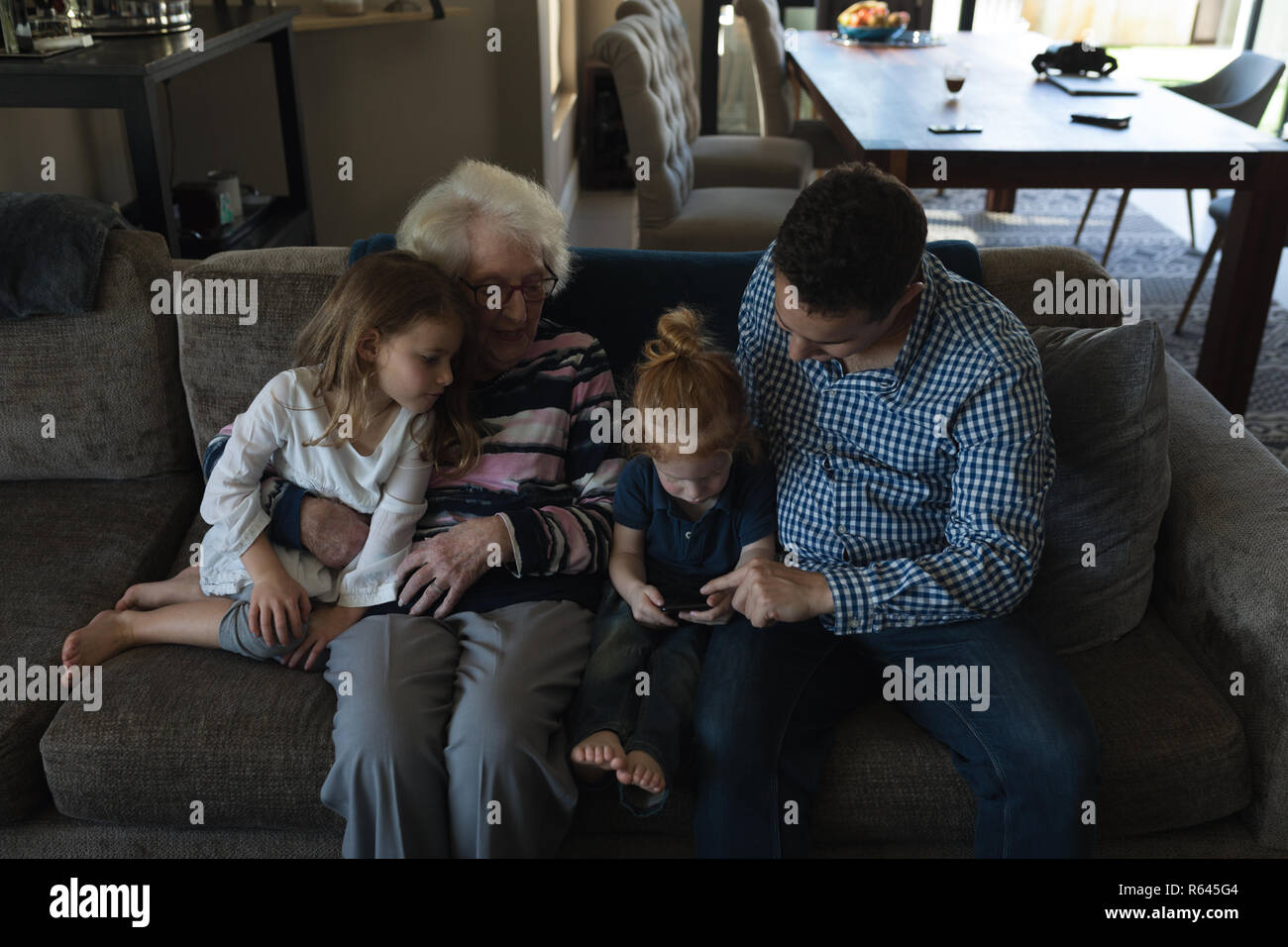 Multi generation family using mobile phone on sofa in living room Stock Photo