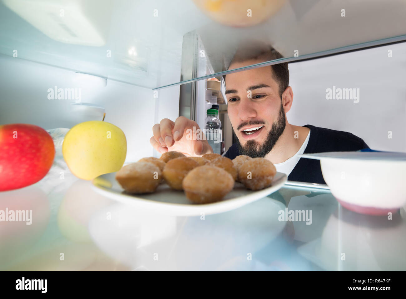 Man Taking Cookie From Plate In Refrigerator Stock Photo