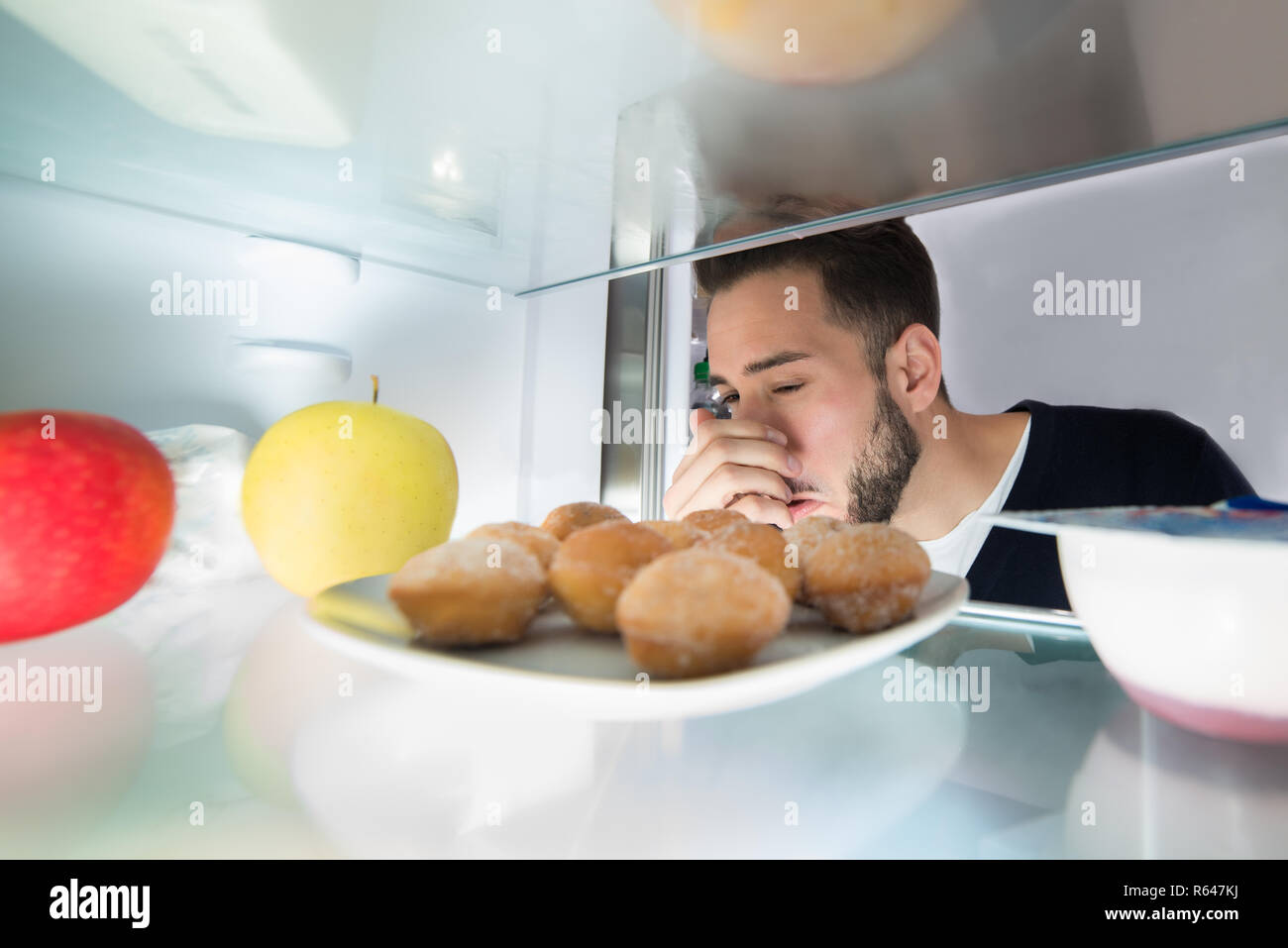 Man Holding His Nose Near Foul Food In Refrigerator Stock Photo