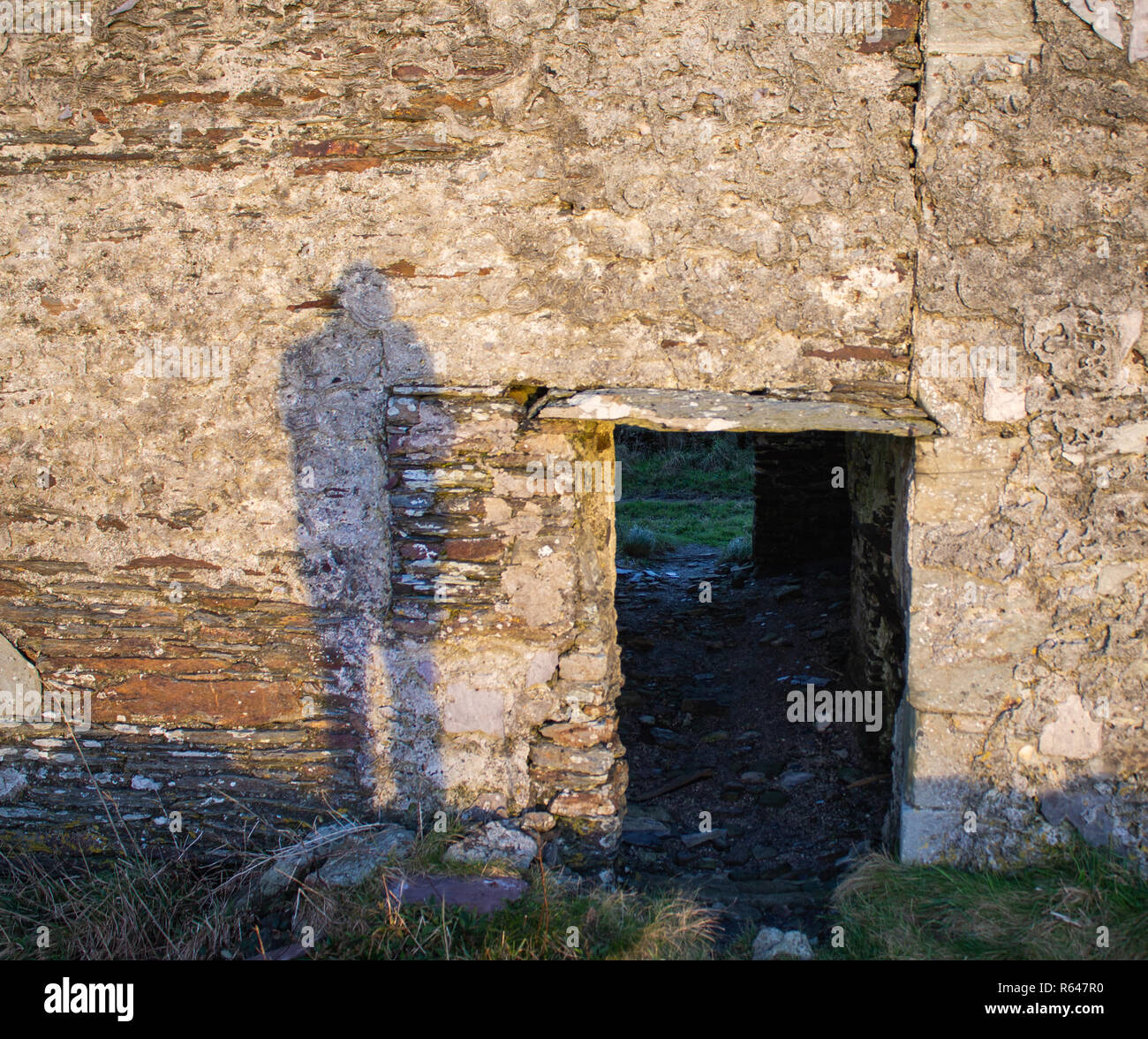 sinister shadow cast next to a stone doorway on a stone wall at sunrise. Stock Photo