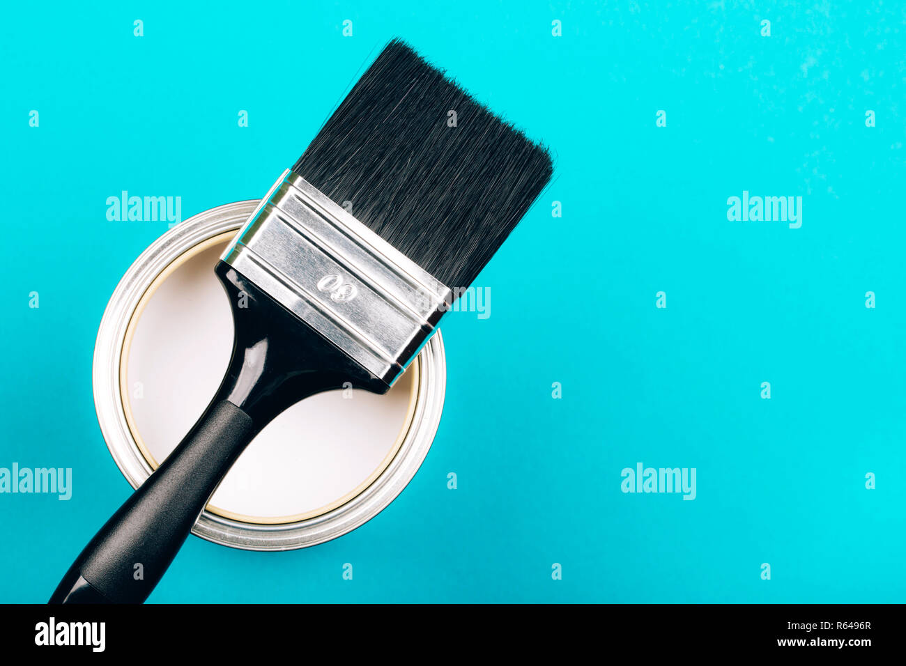 Brush with black handle on open can of white paint on blue background ...