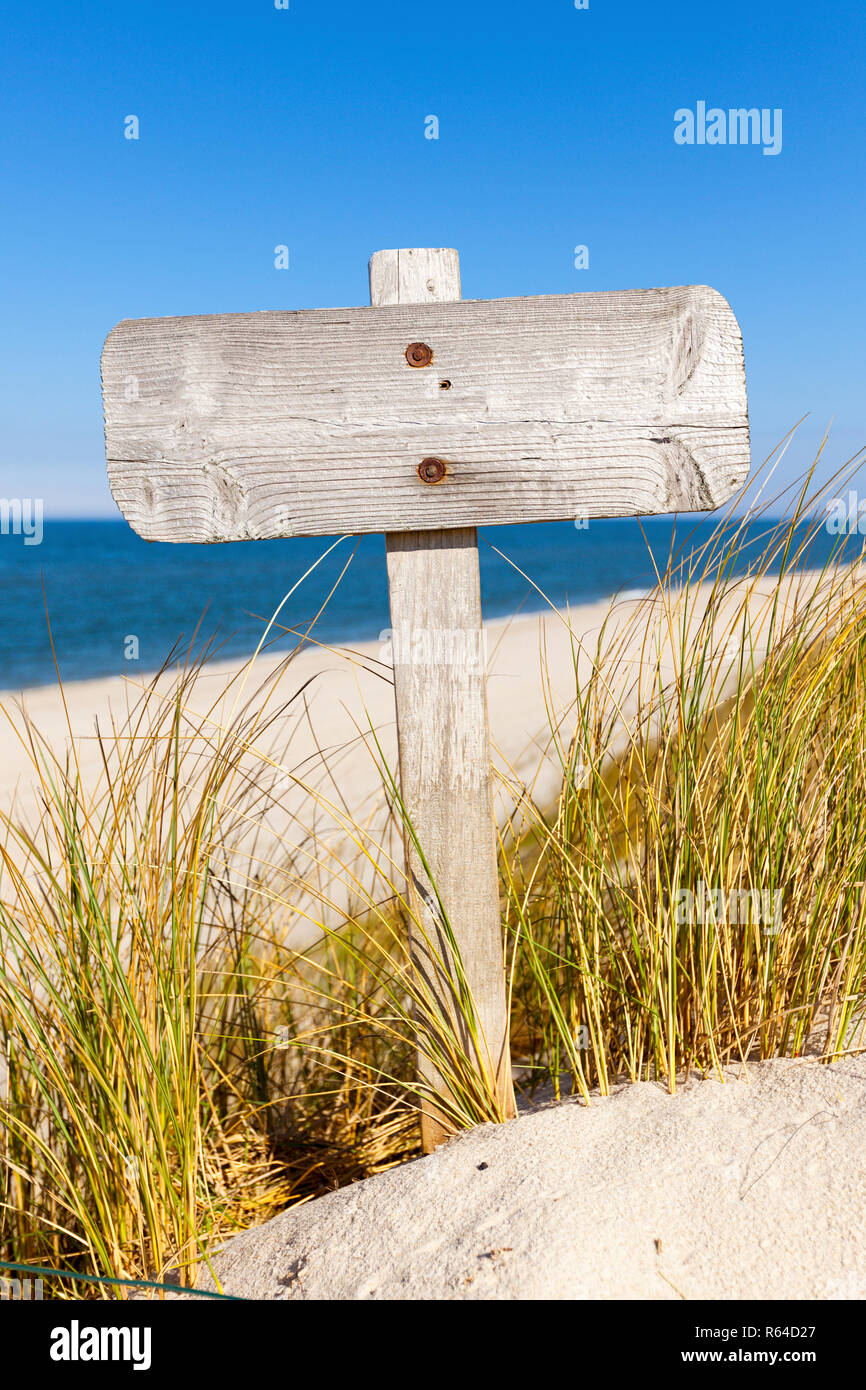 Weathered blank wooden sign between dune grass at the beach Stock Photo