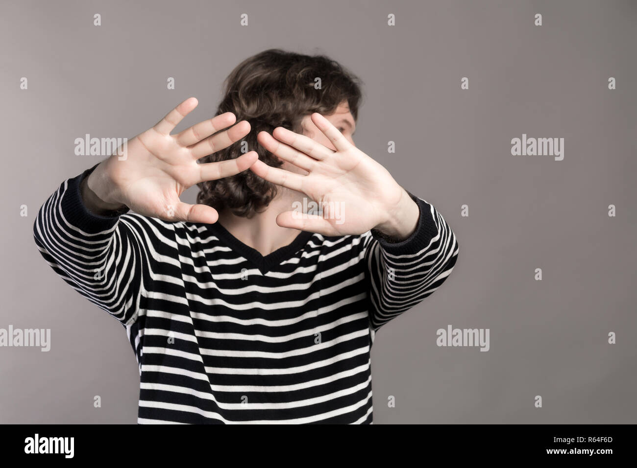 Man in striped sweater turns aside, stretching his hands forward. Pushing someone away from contact. Guy making stop hand sign palm gesture on grey ba Stock Photo