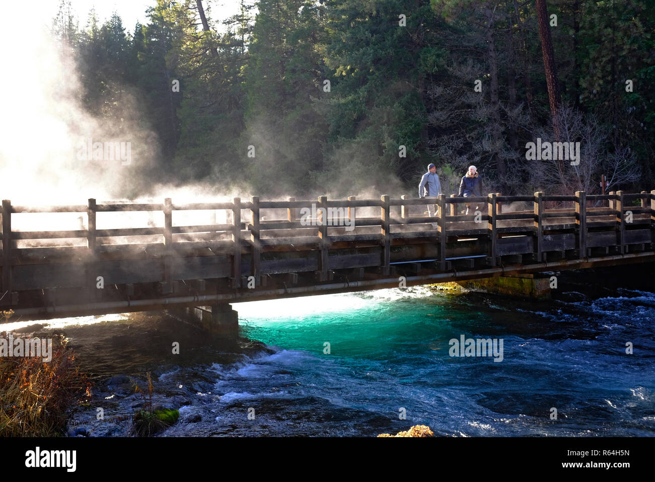 A morning mist rises from the Metolius River in the Cascade Mountains of Oregon, while two hikers enjoy the view. Stock Photo