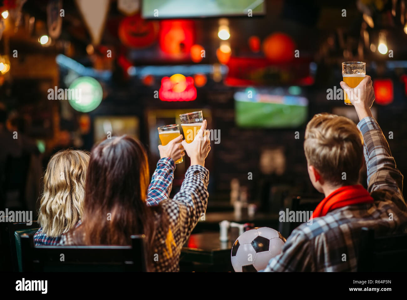 Group of football fans with scarf and ball watching match and drinks beer in sports bar