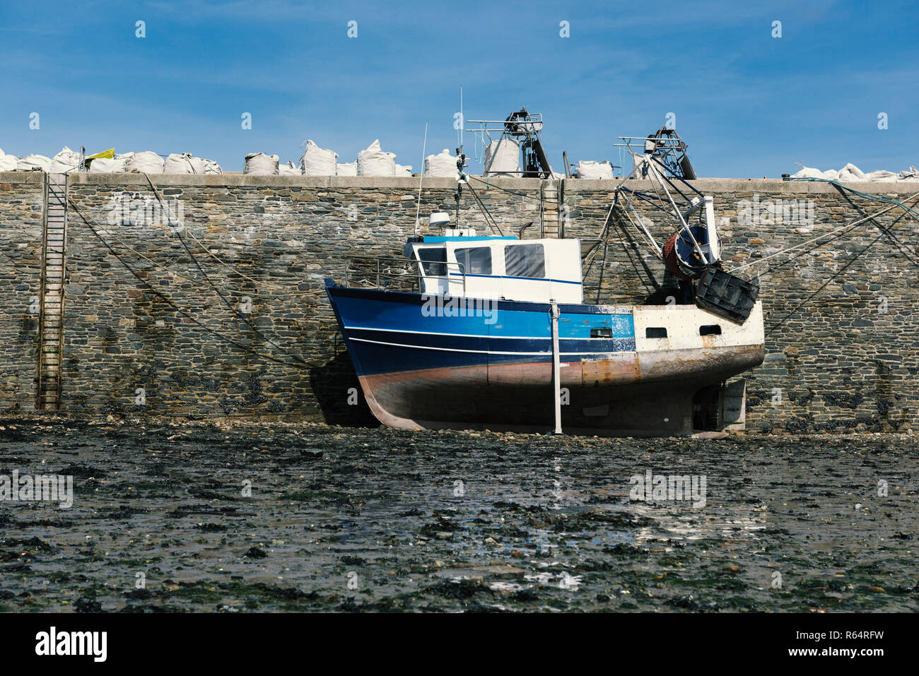 A blue fishing boat is on dry ground in the harbor at low tide Stock Photo