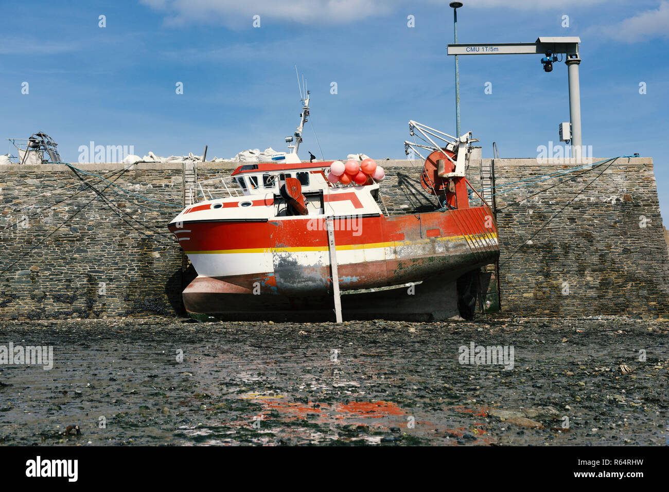 A red fishing boat is on dry ground in the harbor at low tide Stock Photo