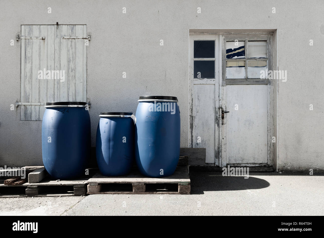 Three blue plastic barrels on a wooden pallet outside. Stock Photo