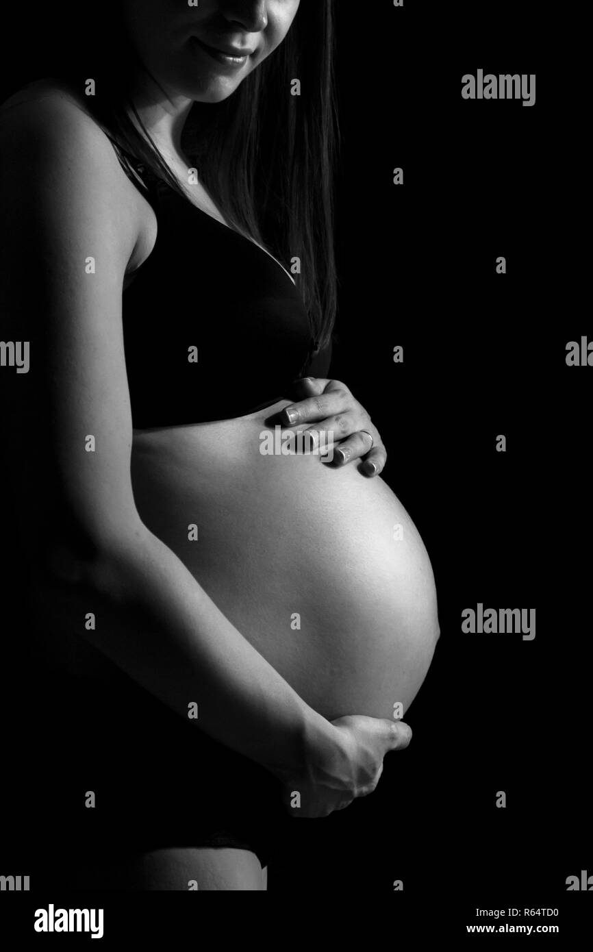 Pregnant woman caressing her belly isolated on black monochrome background. Stock Photo