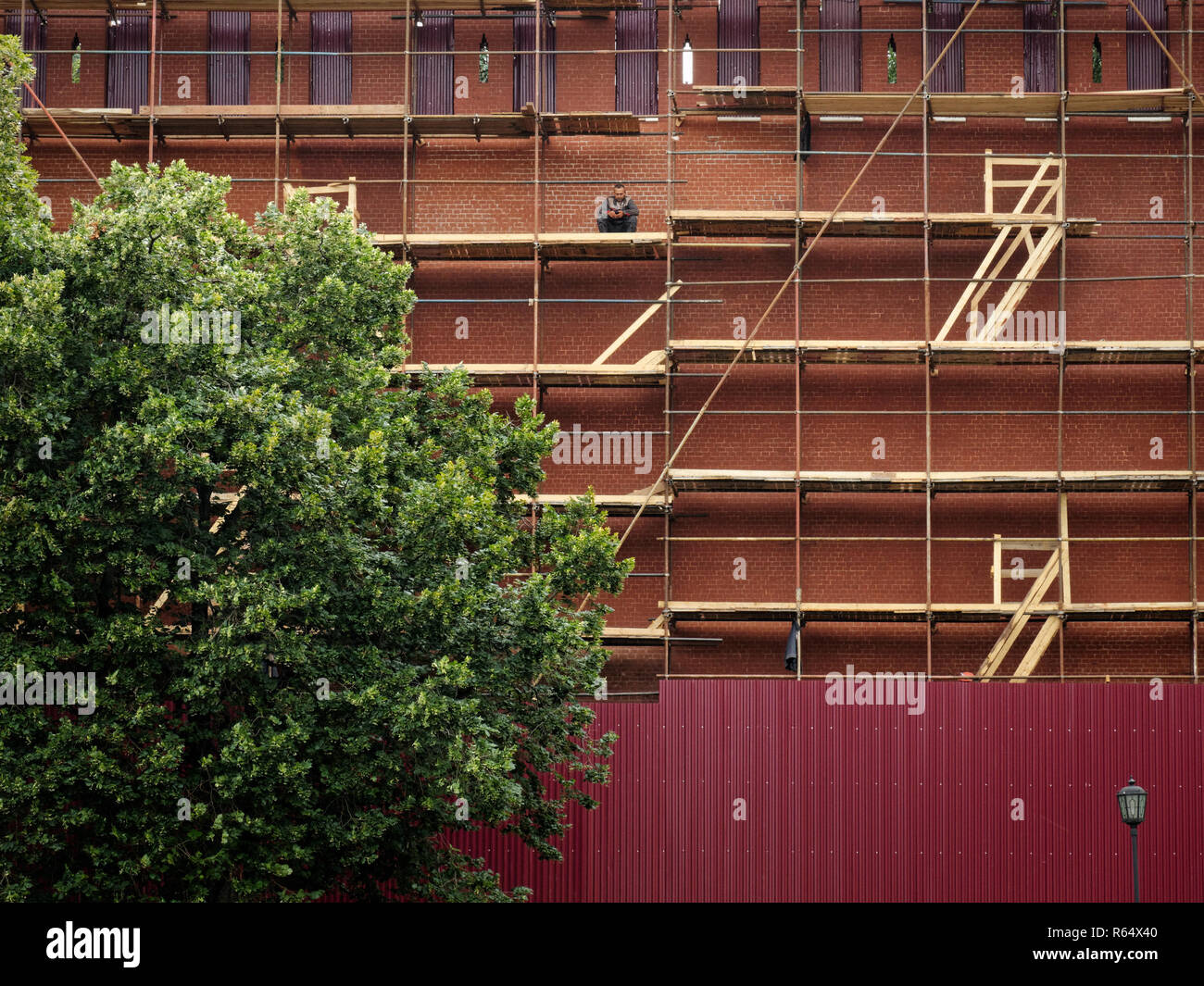Backgrounds and textures: red bricks wall renovation, construction worker sitting lonely at scaffolding Stock Photo