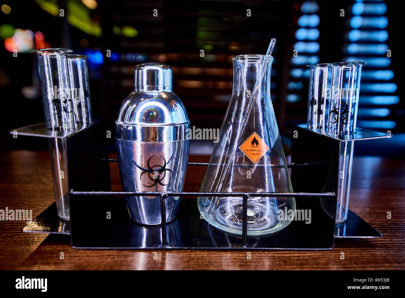 Shaker, flask and test tubes with the symbol of biological hazard, flammable liquid and radiation on a metal rack. Stock Photo