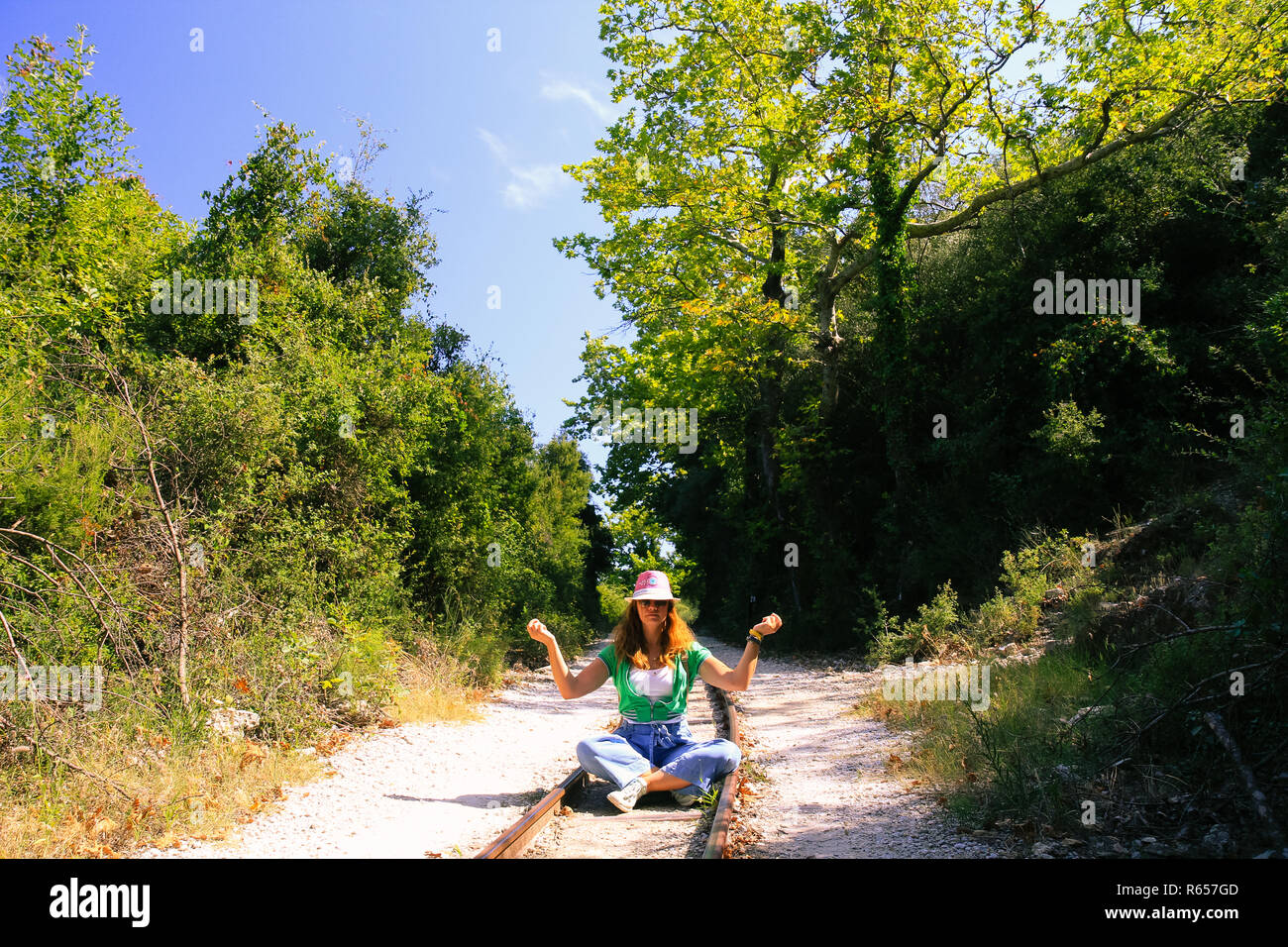 A woman sitting with crossed legs on the rail tracks and practicing yoga. Stock Photo