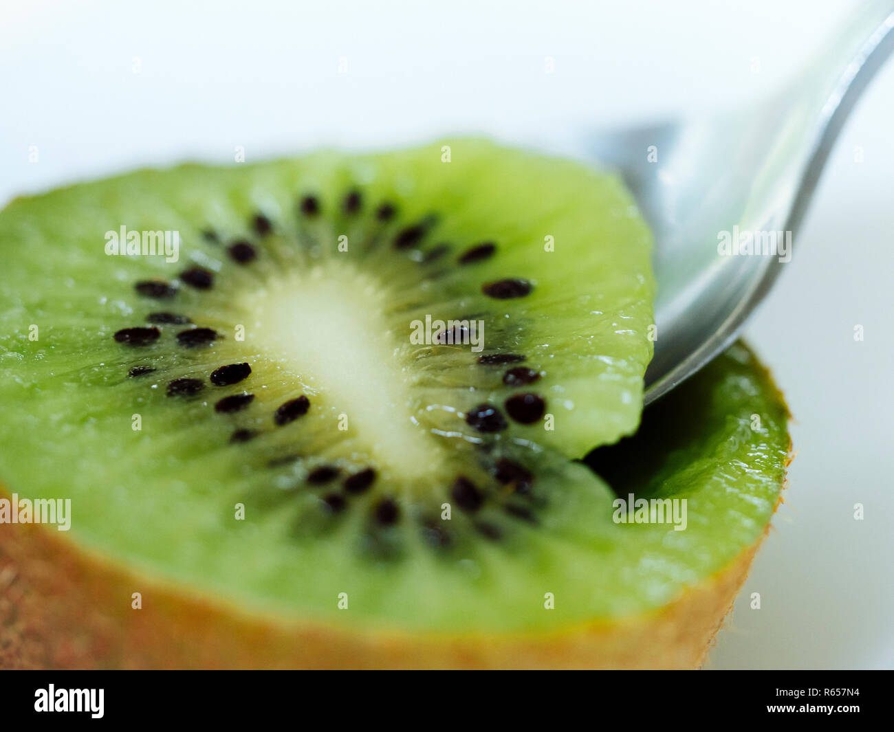 Close up of spoon taking centre of freshly cut kiwi fruit Stock Photo