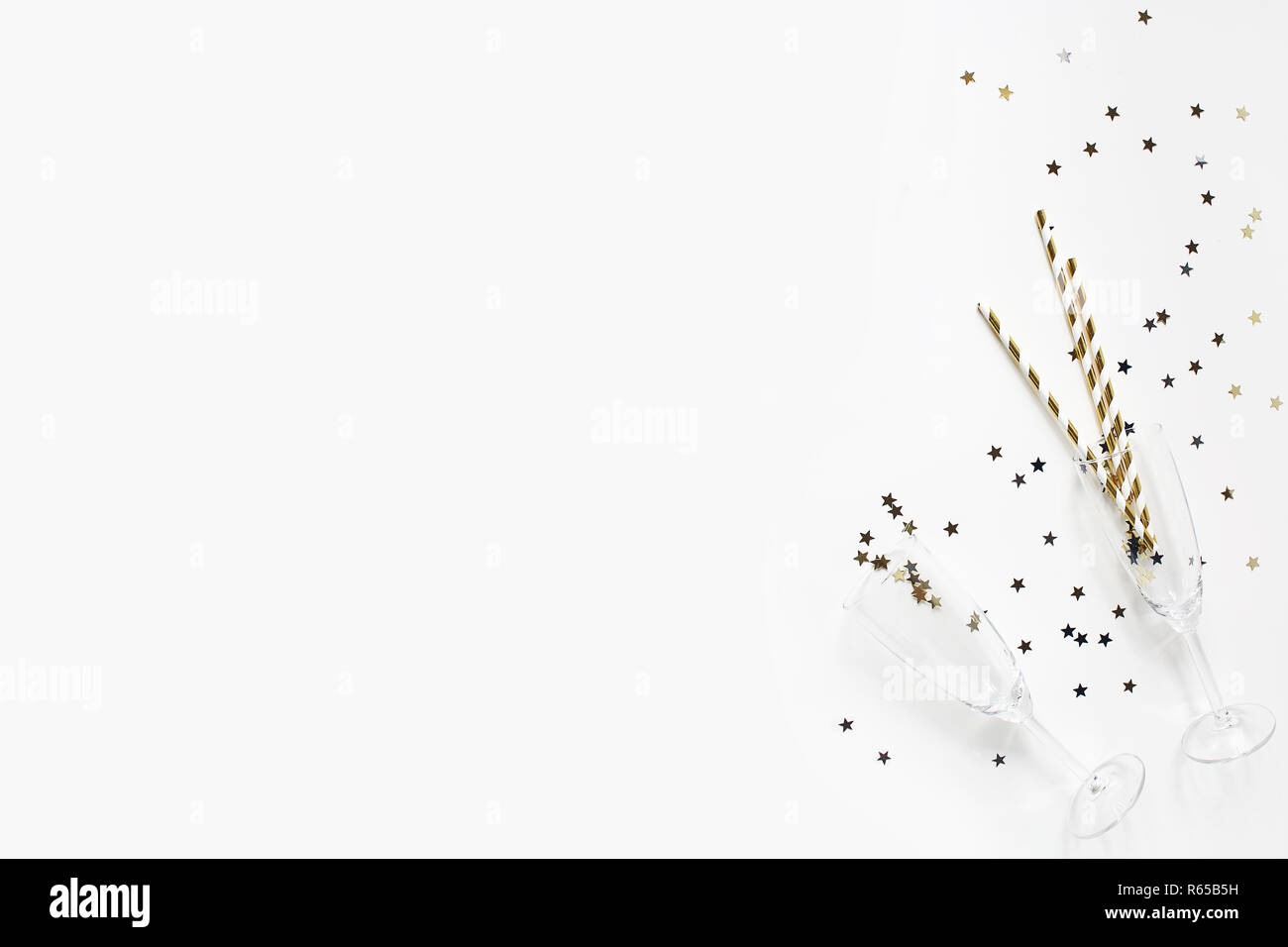 Happy New Year composition. Champagne glasses with golden confetti stars and drinking straws isolated on white table background. Celebration, party concept. Flat lay, top view. Empty copy space. Stock Photo