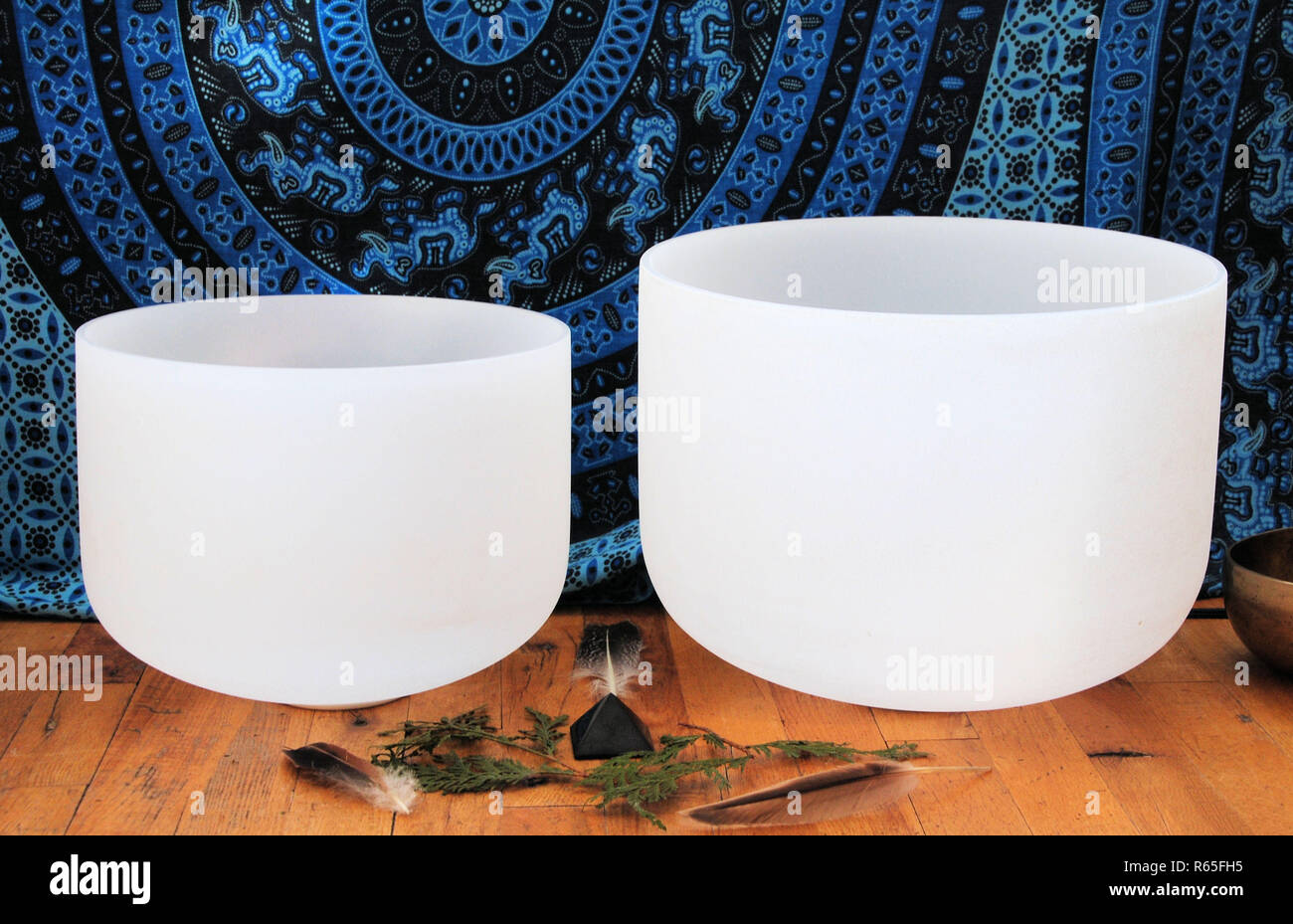 Two white crystal singing bowl on a wooden floor with an altar and a blue Indian type of linen decoration in the background Stock Photo