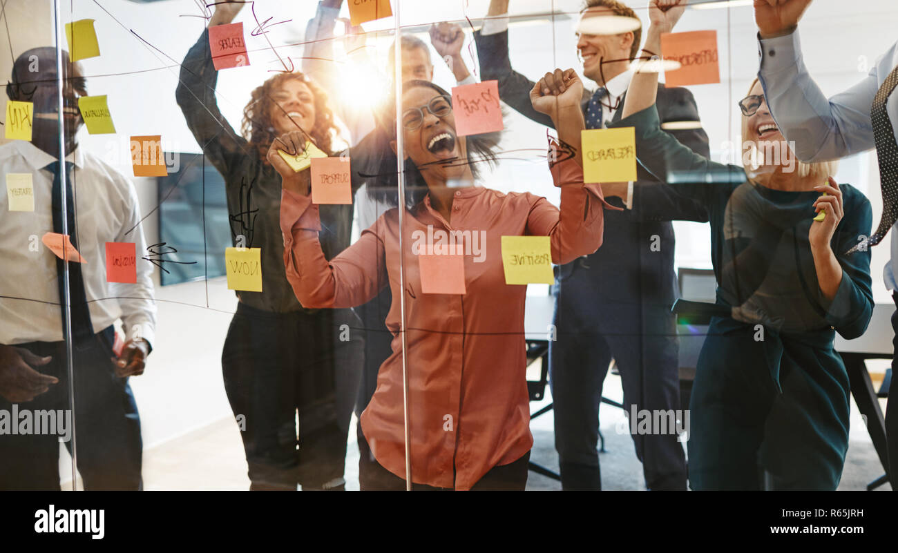 Group of ecstatic businesspeople cheering and jumping up and down while celebrating after a brainstorming session with sticky notes in an office Stock Photo