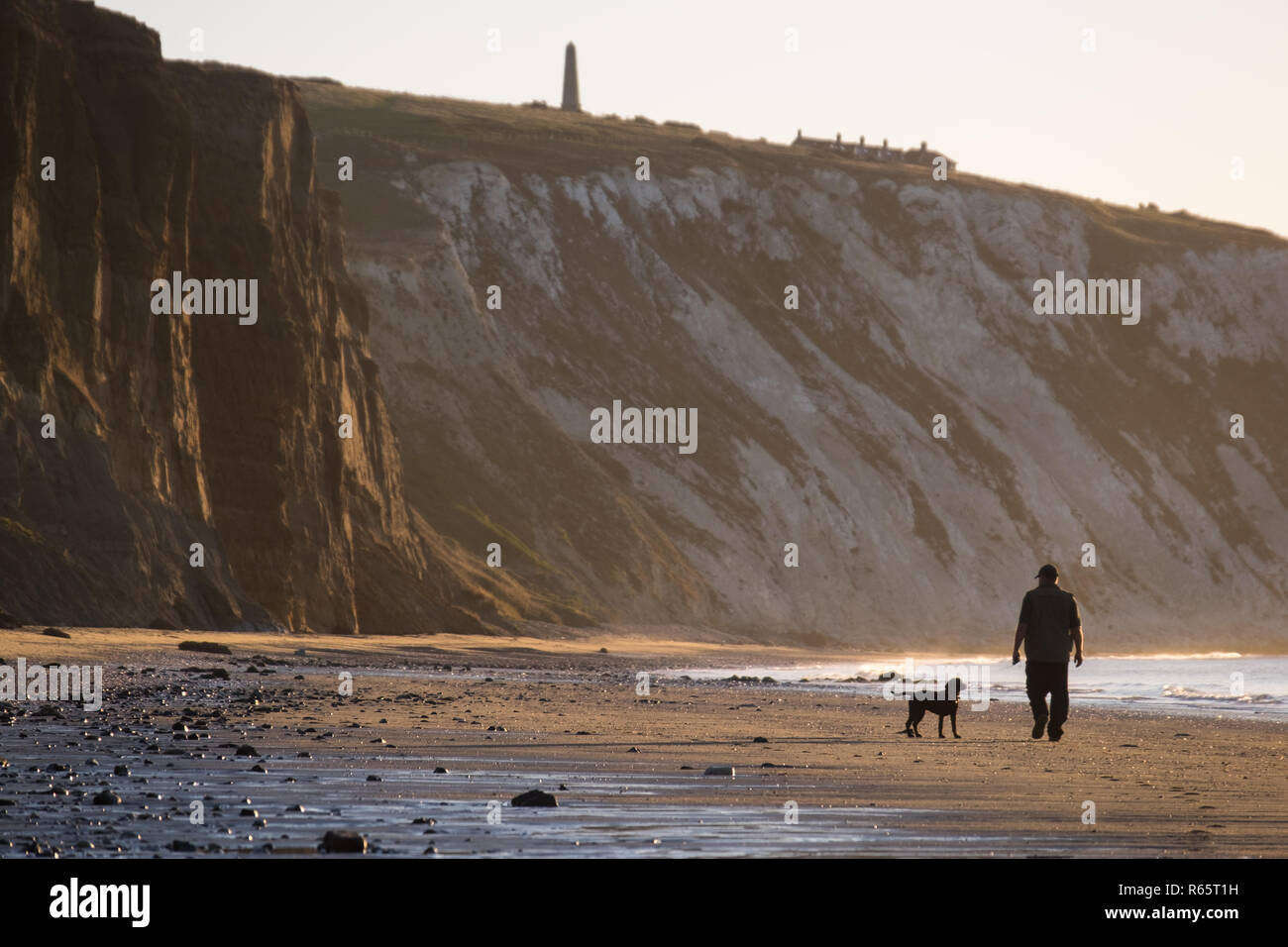 A man walking his dog during sunrise at Yaverland Beach on the Isle of Wight, UK Stock Photo