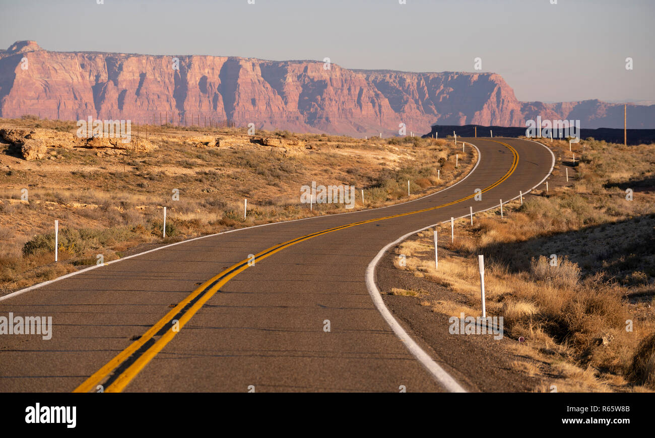 The sun hits golden rock buttes behind a rise and bend in the road desert southwest USA Stock Photo