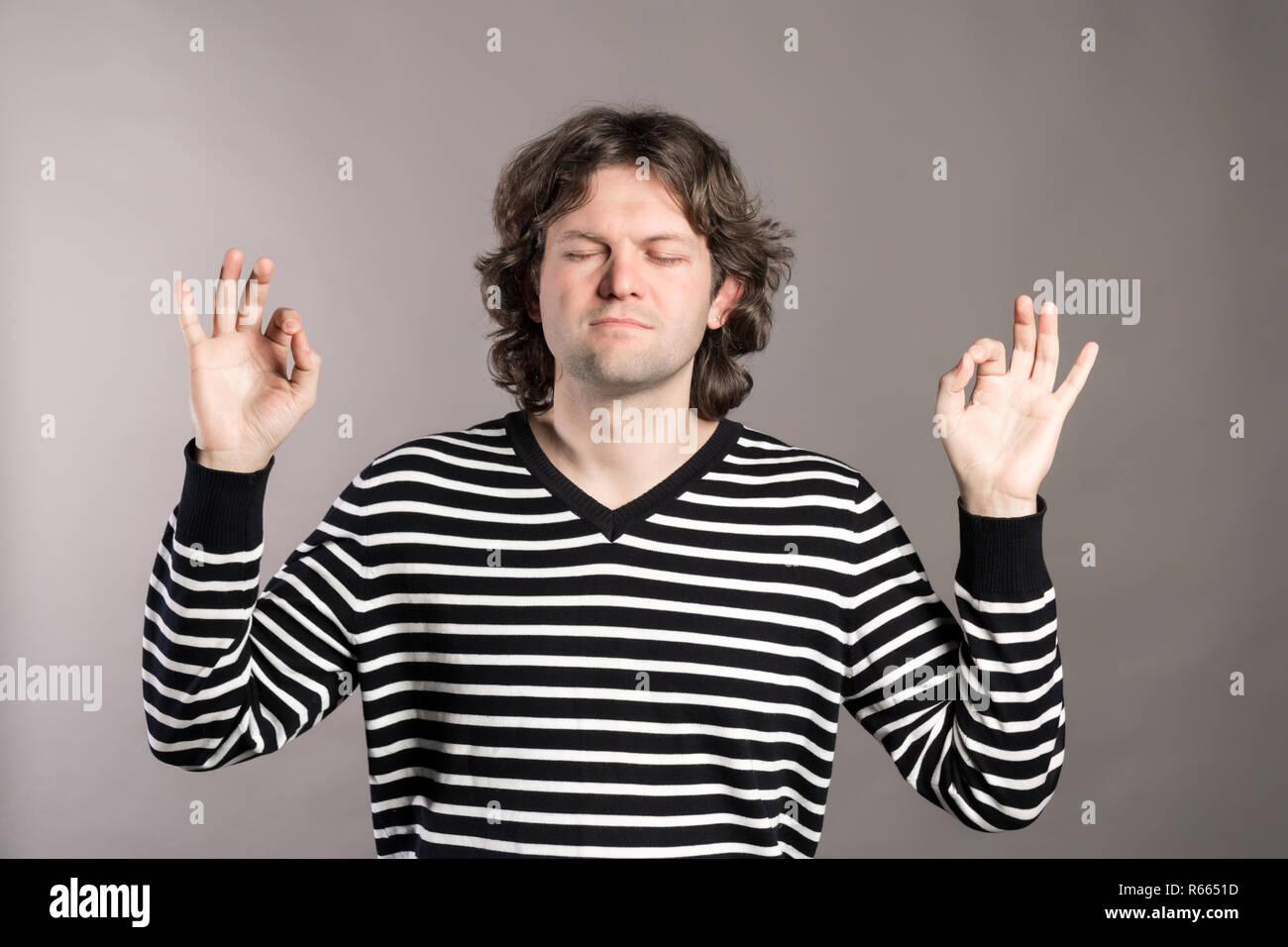 Peaceful young man meditating with his eyes closed and keeping hands in mudra gesture. Handsome guy concentrating. Harmony concept. Isolated front vie Stock Photo