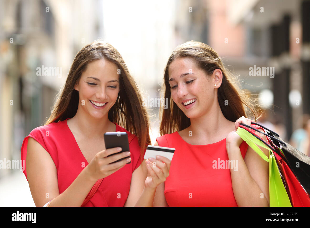 Front view of two happy shoppers buying online with credit card and cellphone walking in the street Stock Photo